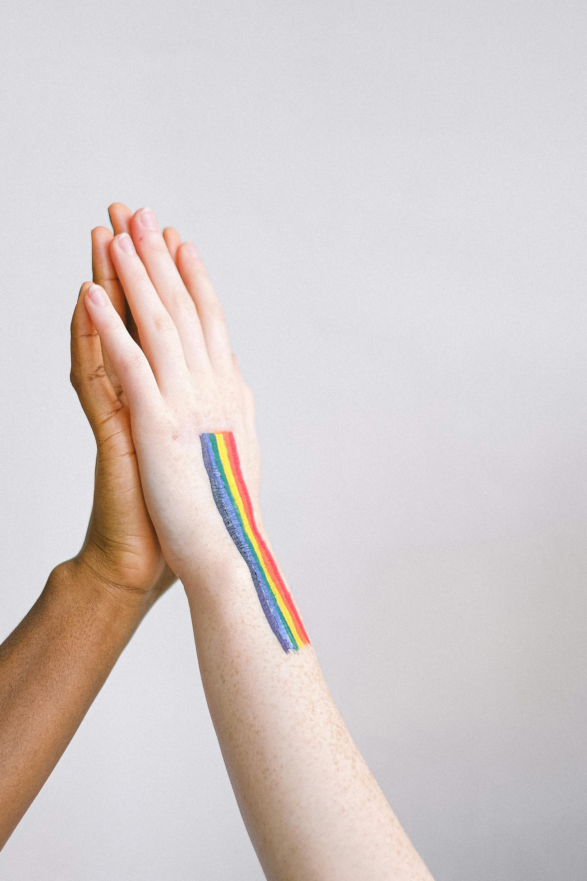 Two hands in a high-five, one with a rainbow stripe on the wrist, against a white background.