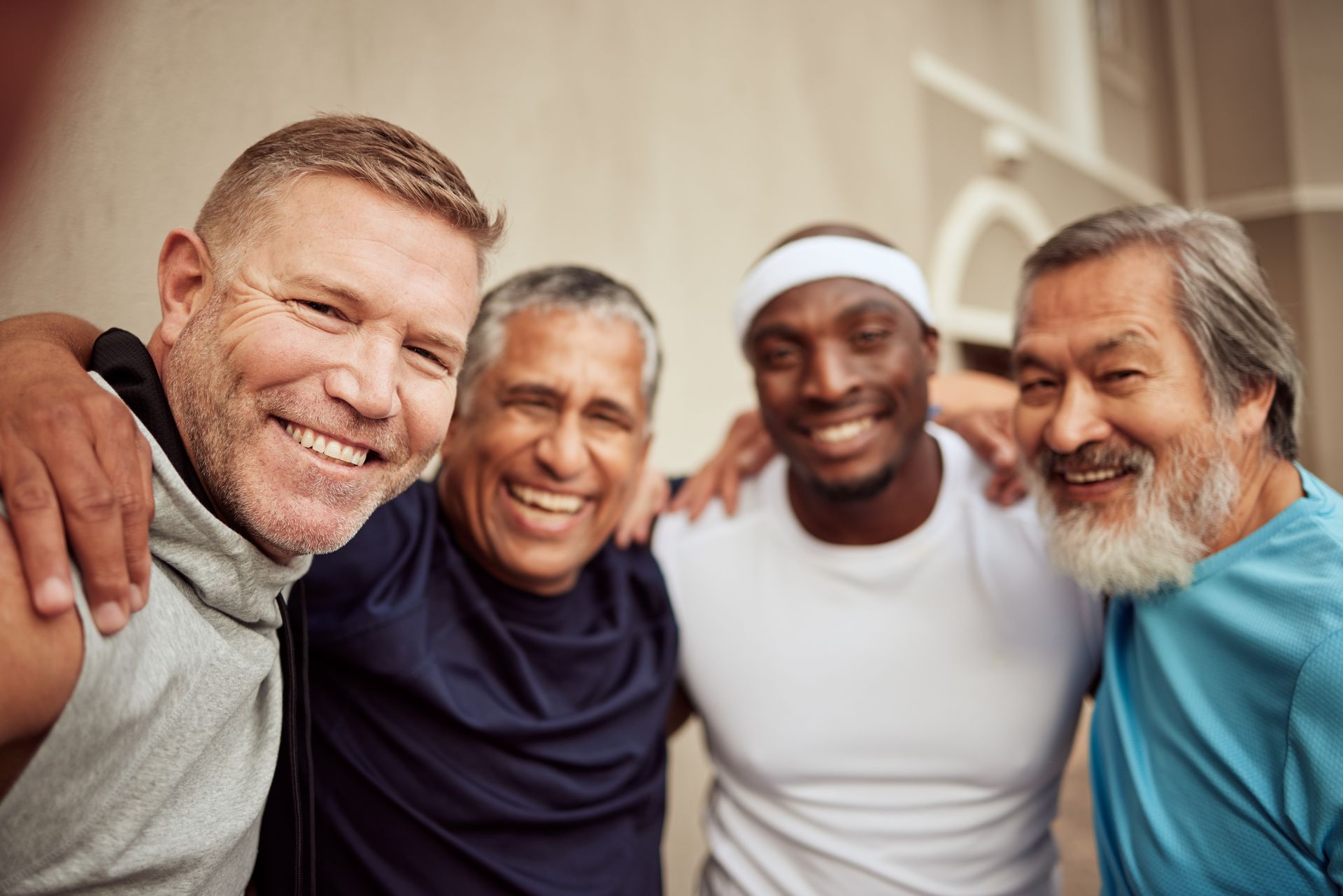 Four people in athletic wear smiling and embracing, outdoors.