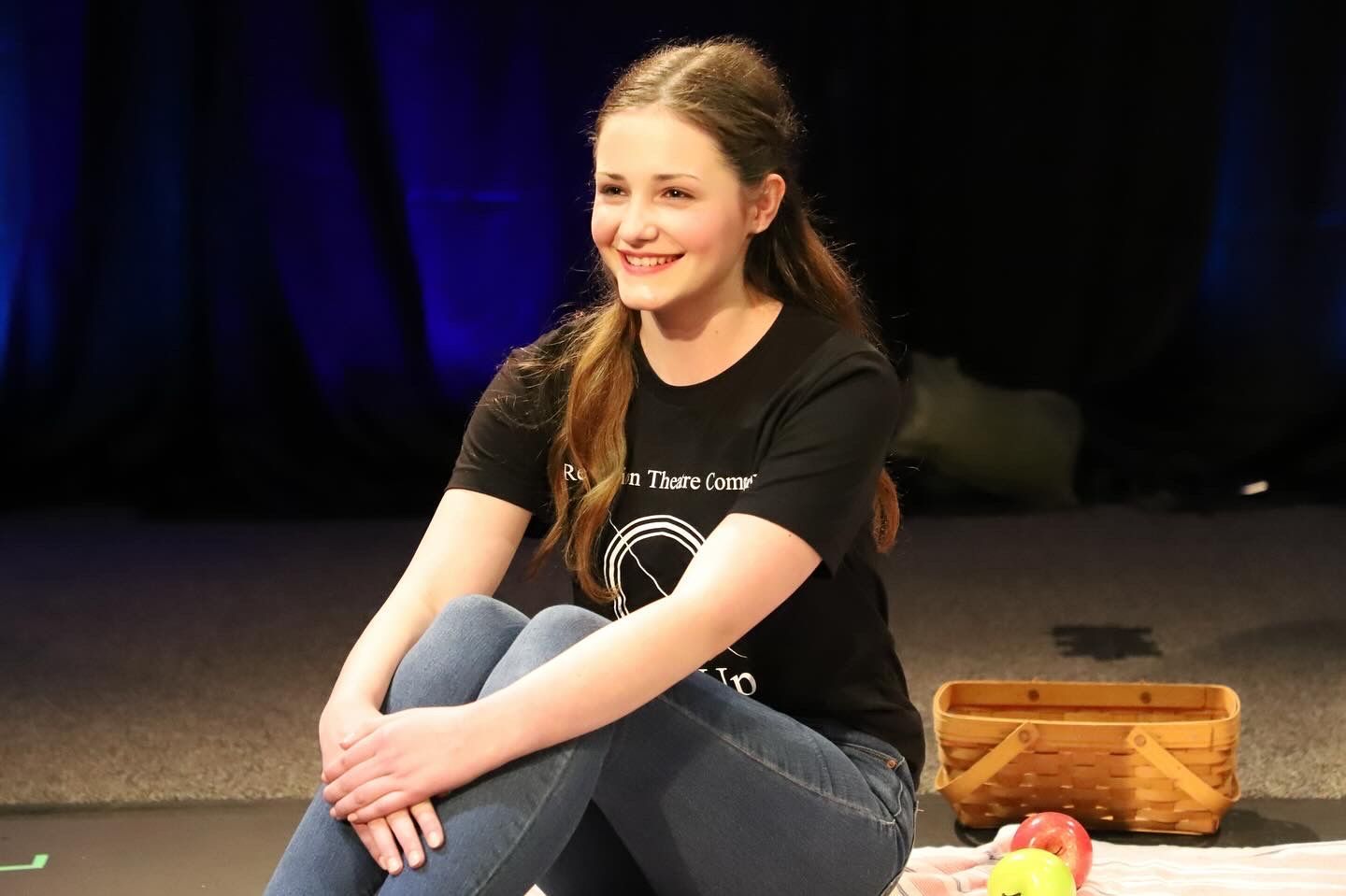 A young woman is sitting on the floor with her legs crossed.