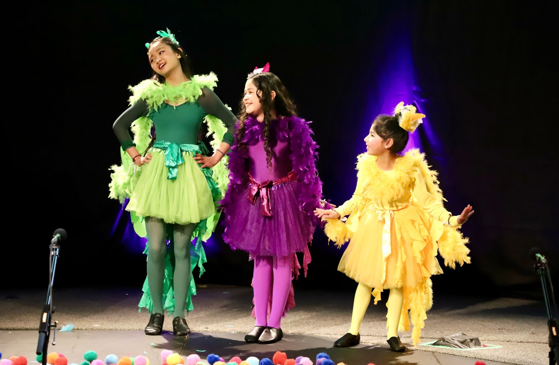 Three little girls in costumes are standing on a stage.