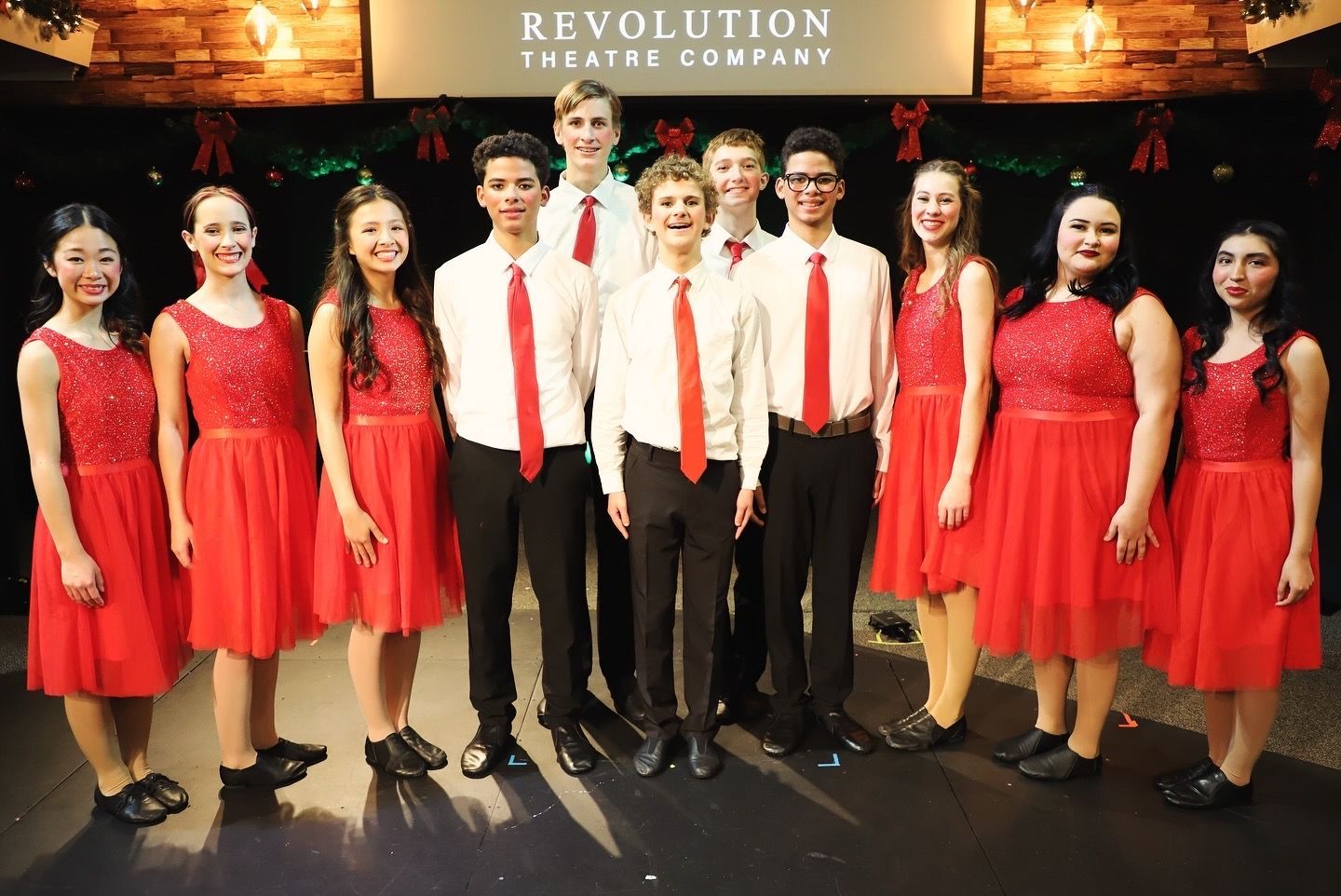 A group of people are posing for a picture in front of a revolution theatre company sign.