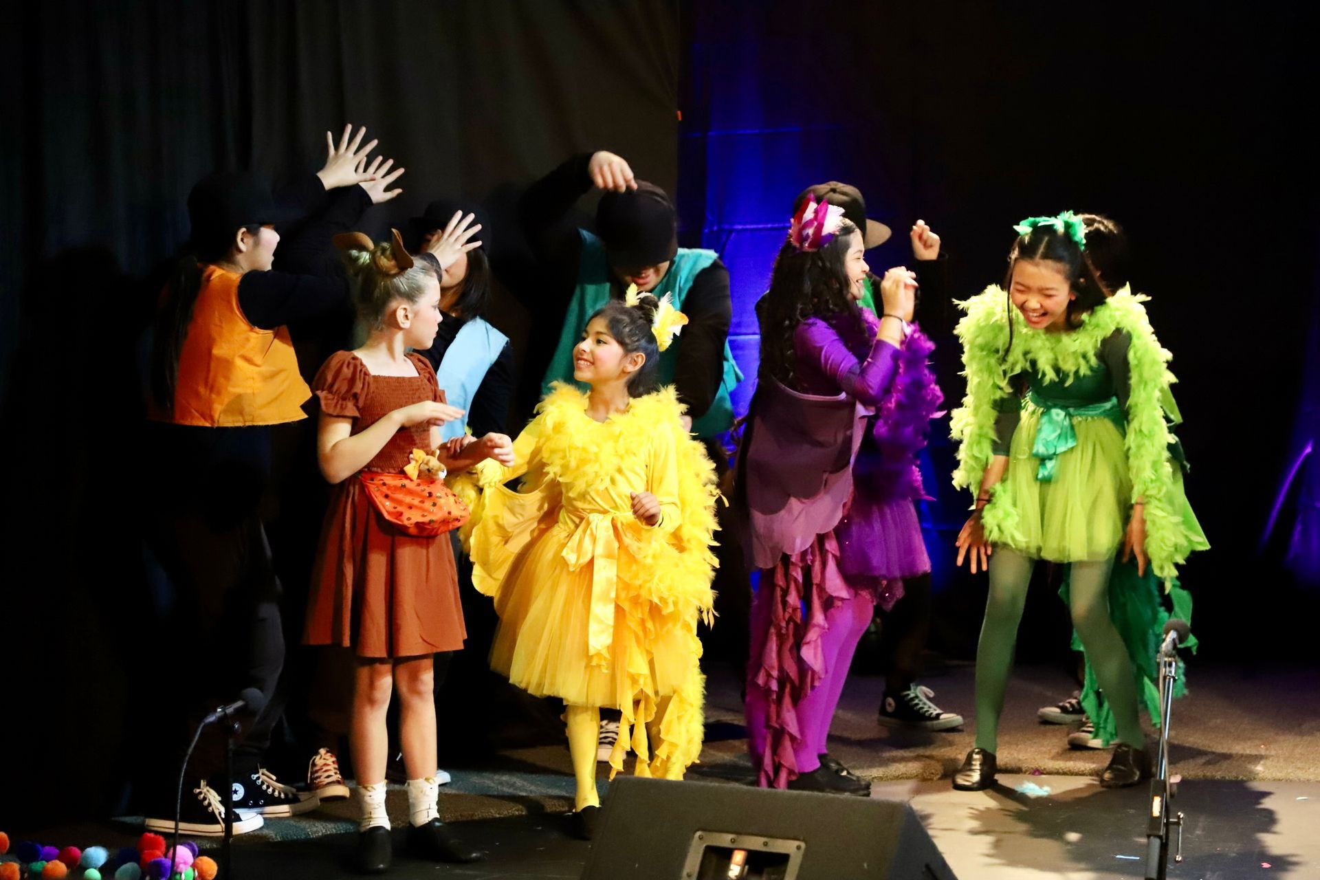 A group of children in colorful costumes are dancing on a stage.