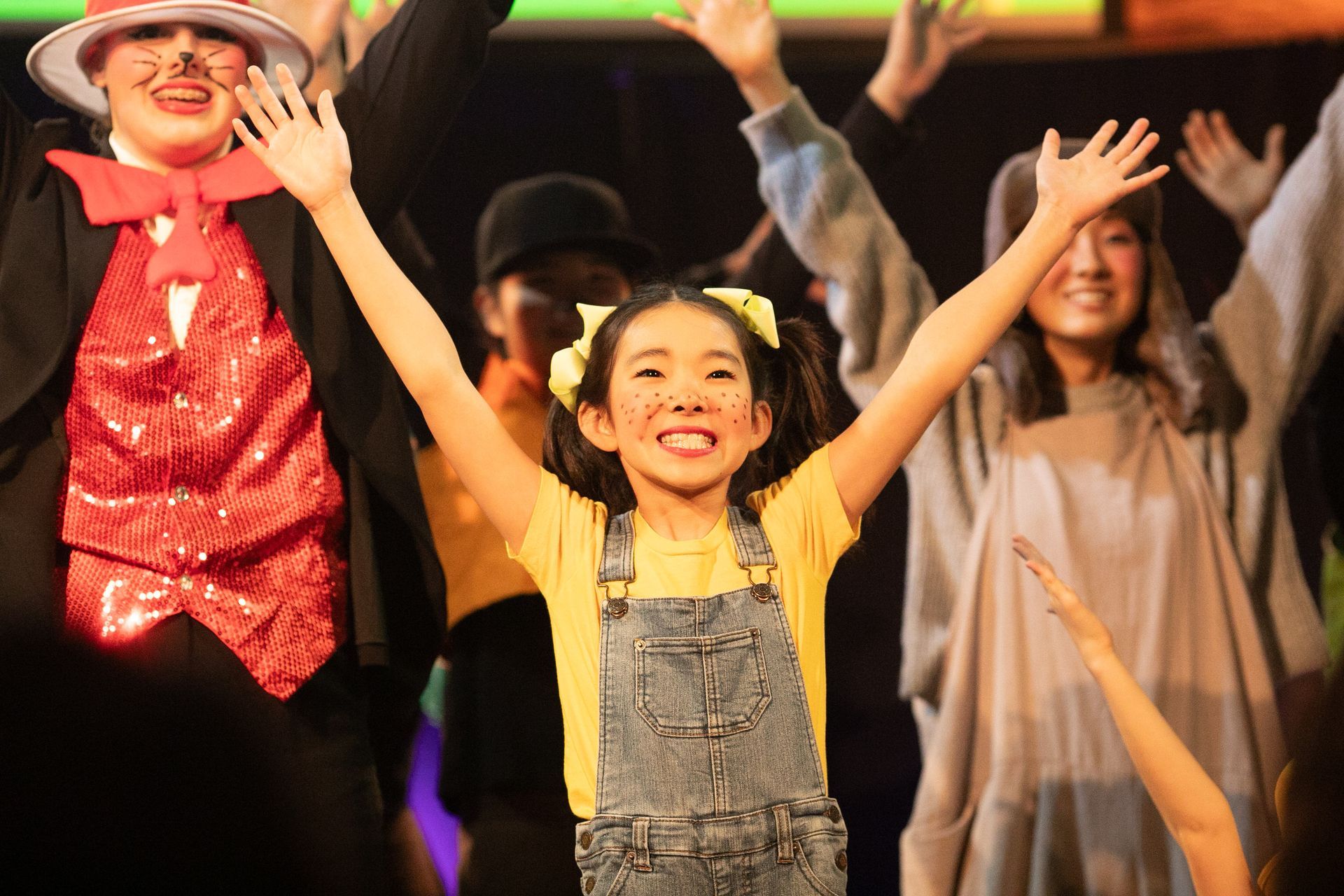 A group of children are standing on a stage with their arms in the air.