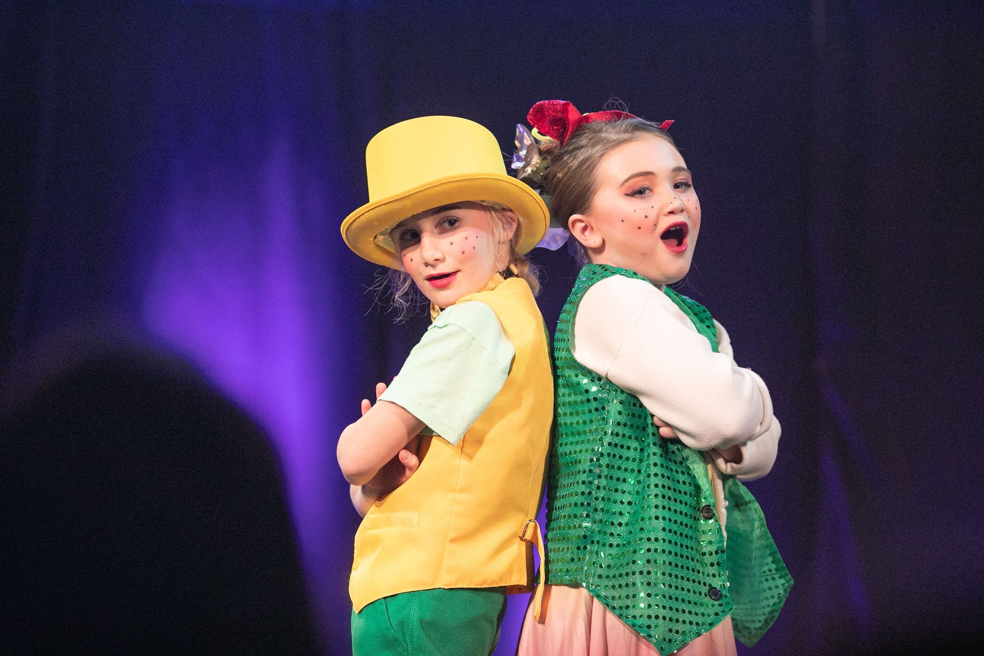 Two young girls are standing back to back on a stage.
