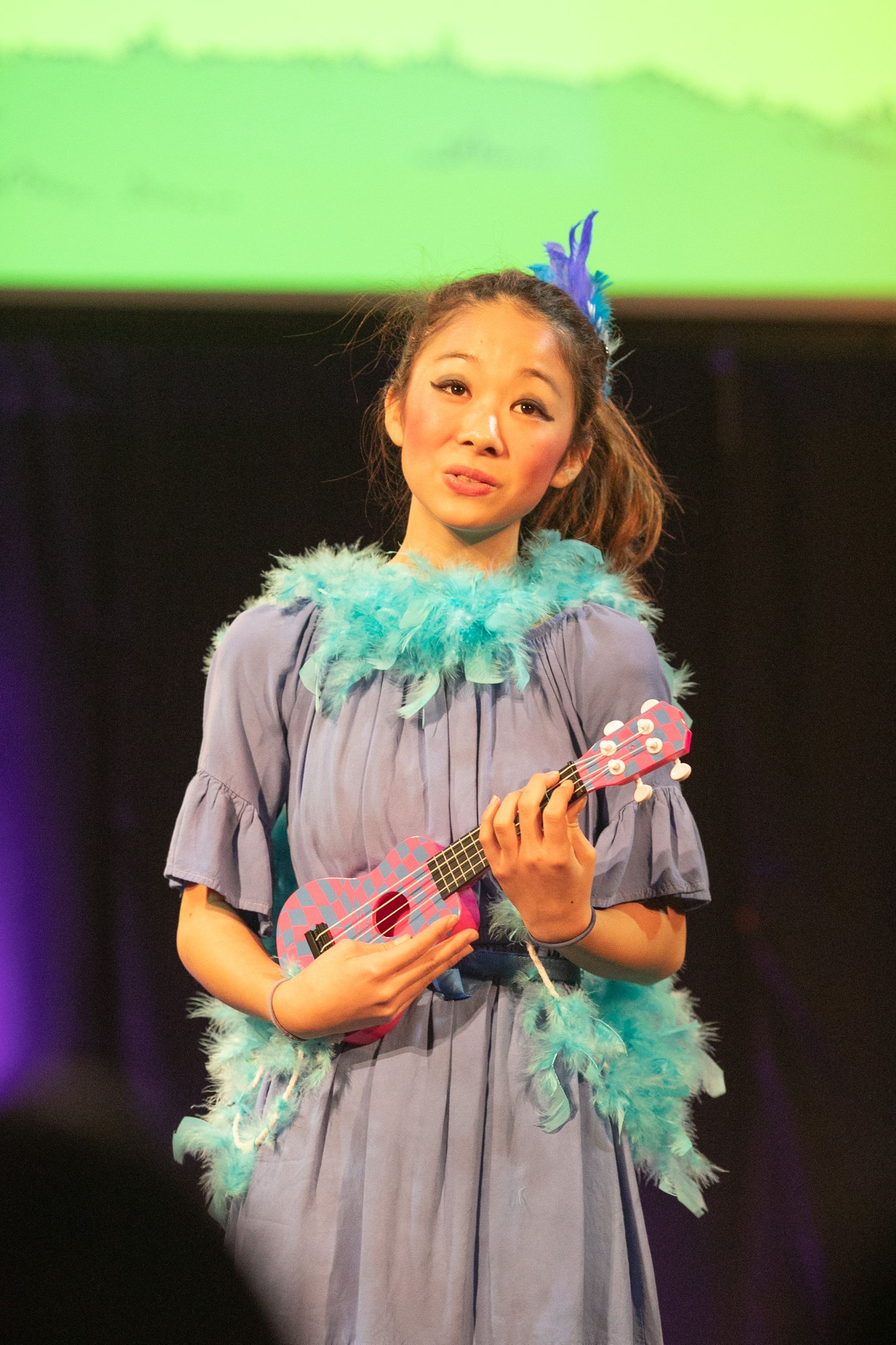A woman in a blue dress is holding a pink ukulele.