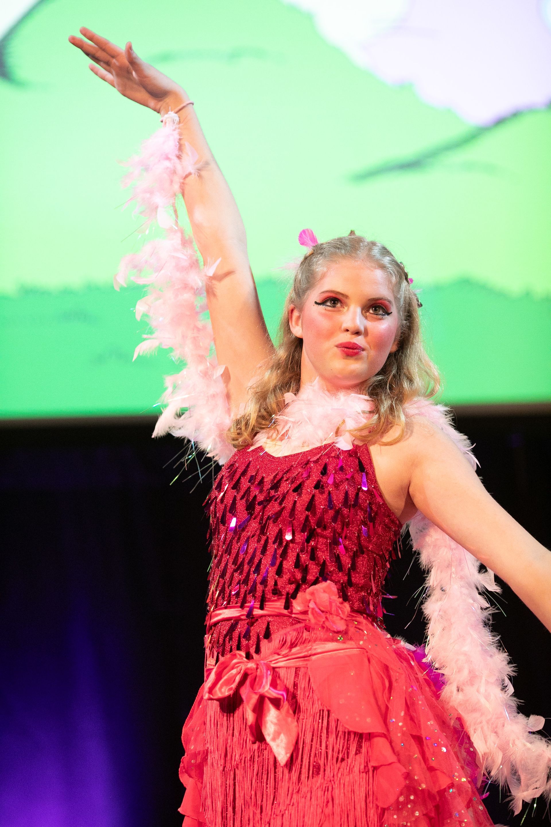 A woman in a red dress and pink boa is dancing on a stage.