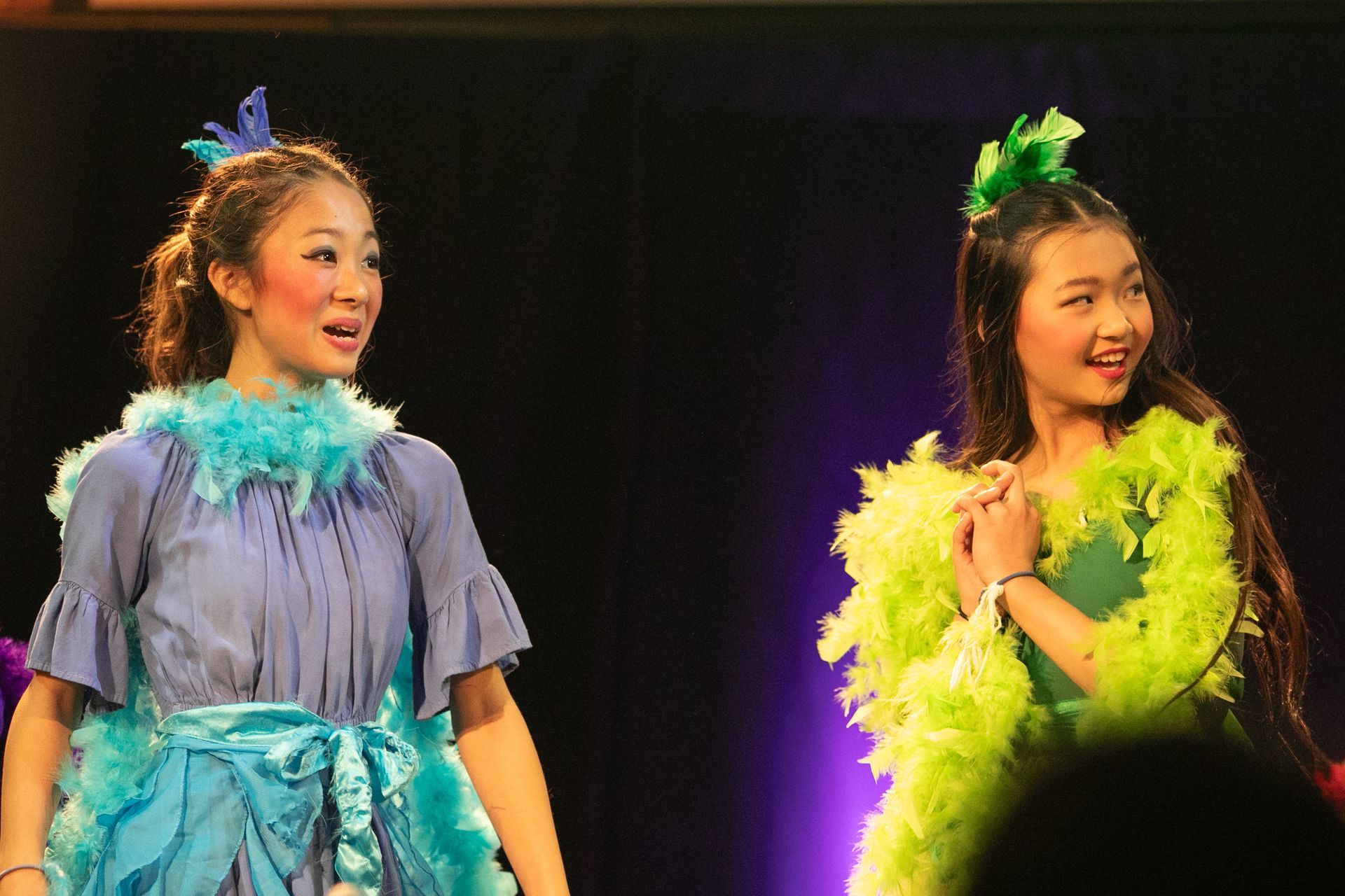 Two women are standing next to each other on a stage and one is wearing a blue dress and the other is wearing a green dress