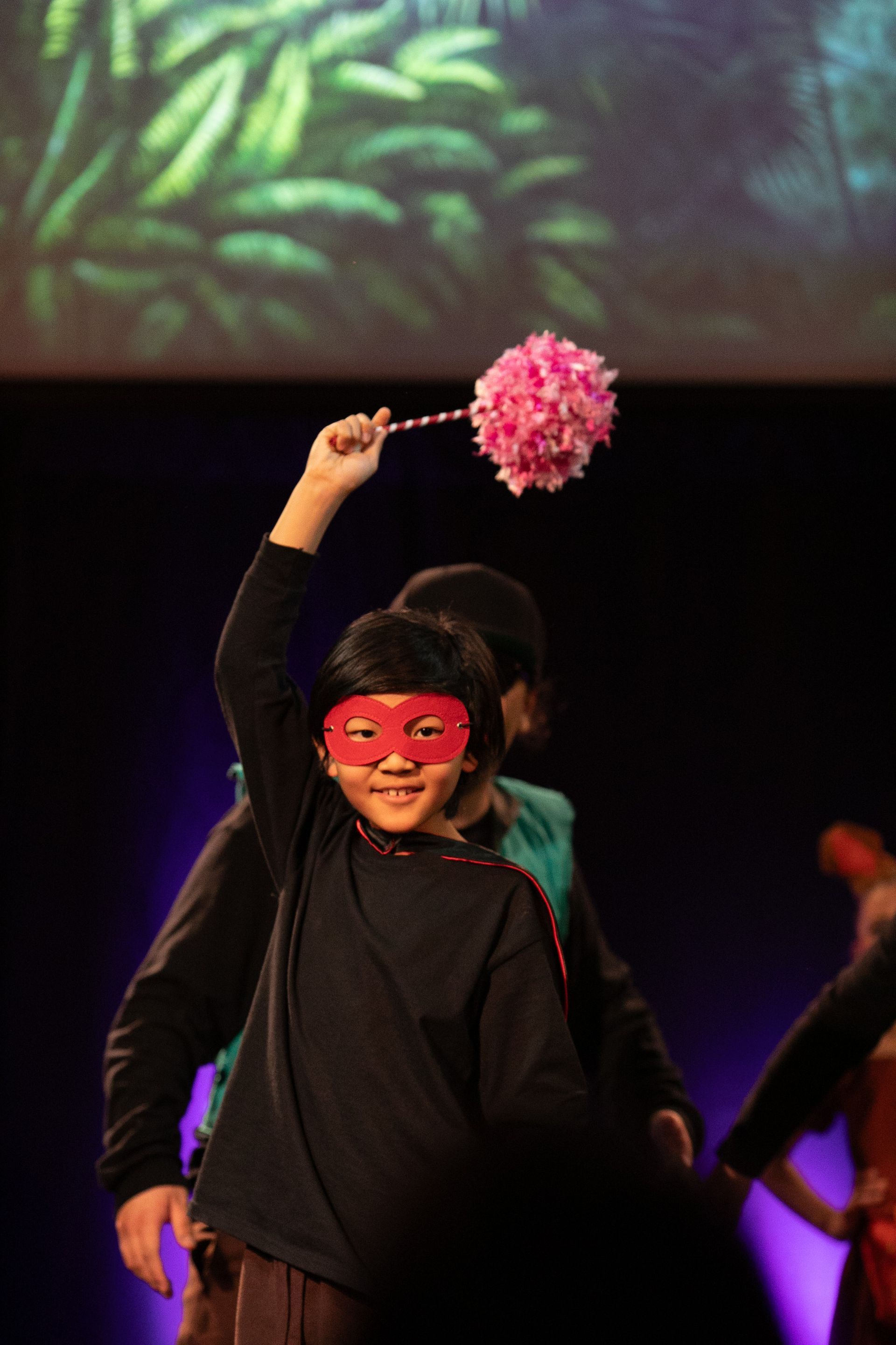 A young girl wearing a mask is holding a pink flower in her hand.