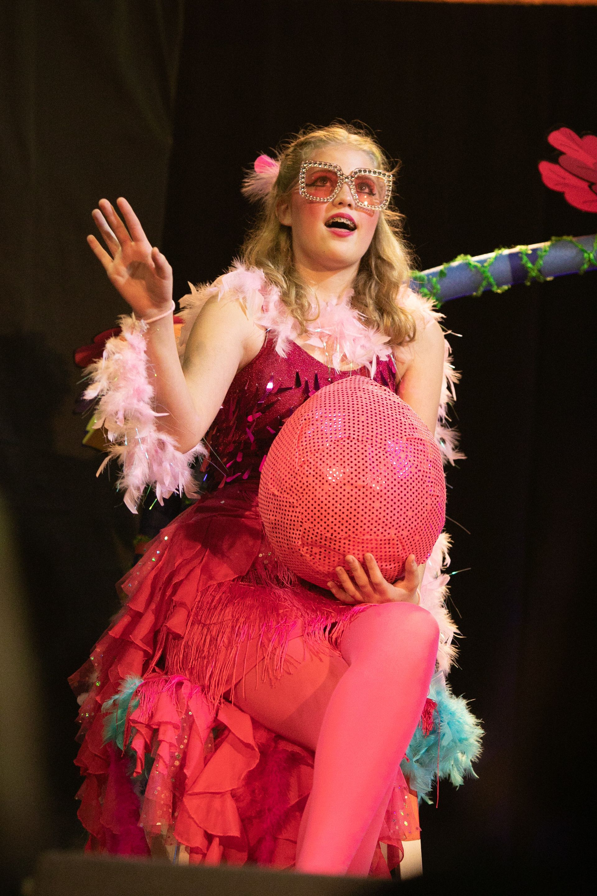 A woman in a pink dress is sitting on a chair holding a pink ball.