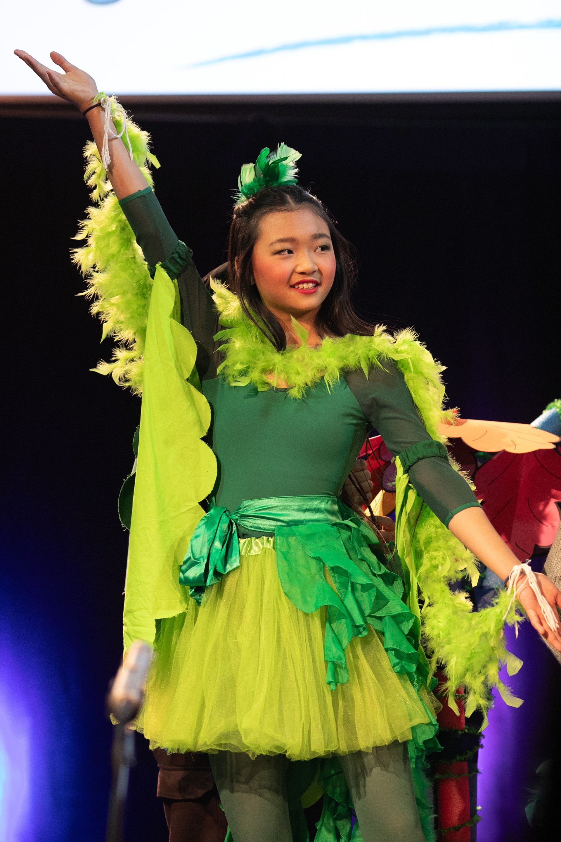 A young girl in a green and yellow costume is dancing on a stage.