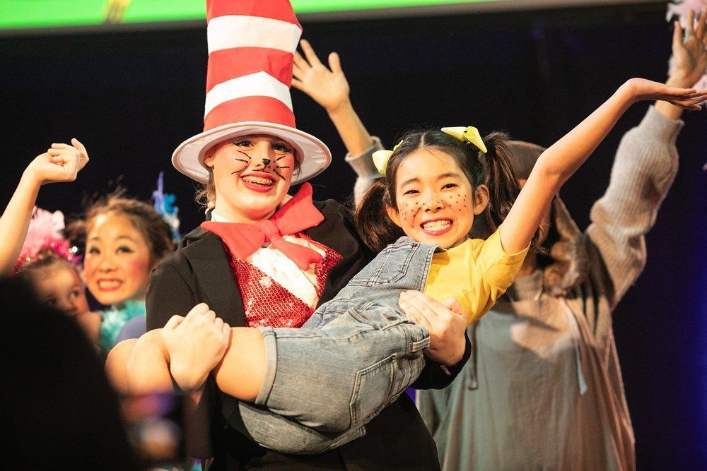 A woman in a cat in the hat is holding a little girl in her arms.