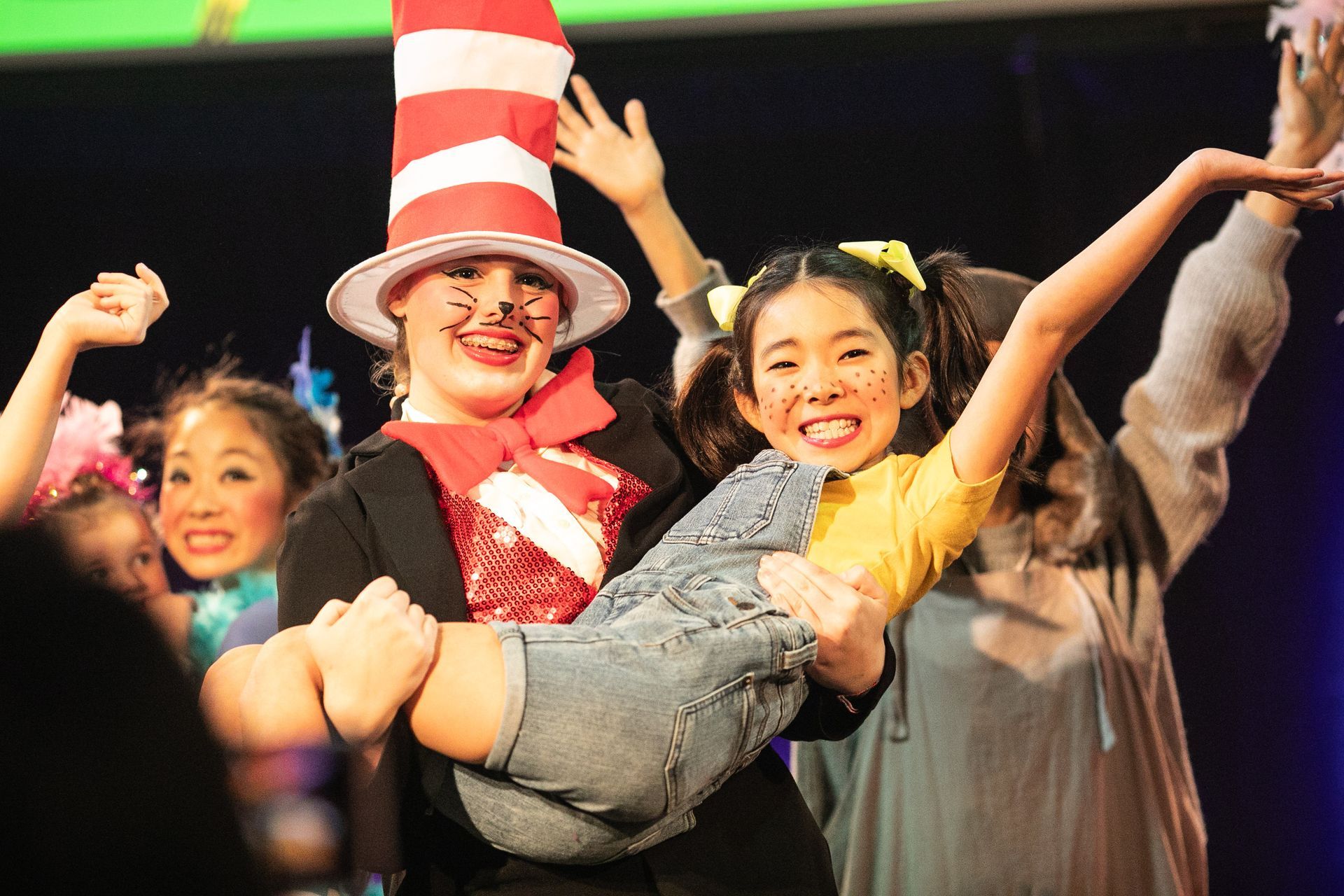 A man in a cat in the hat is holding a little girl in his arms.