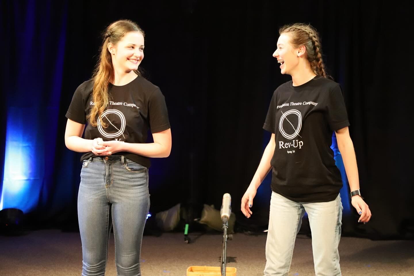 Two young women are standing next to each other on a stage in front of a microphone.