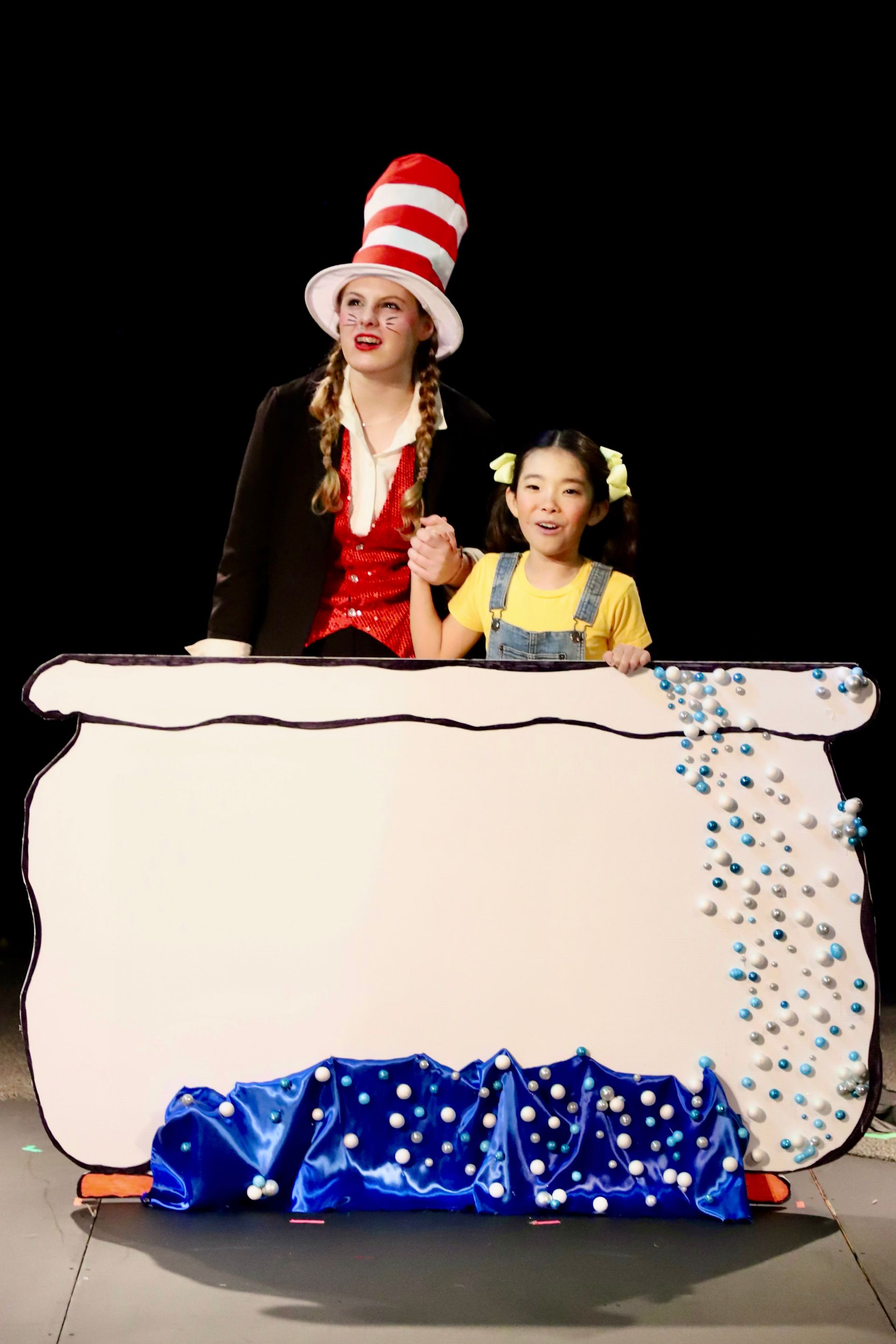 A woman in a cat in the hat is standing next to a little girl.