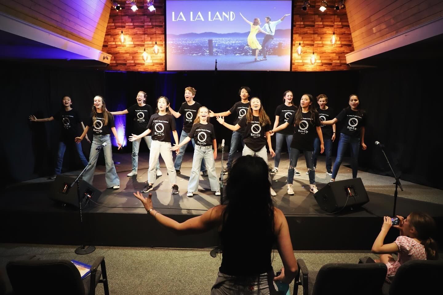 A group of people are dancing on a stage in front of a screen that says la la land.