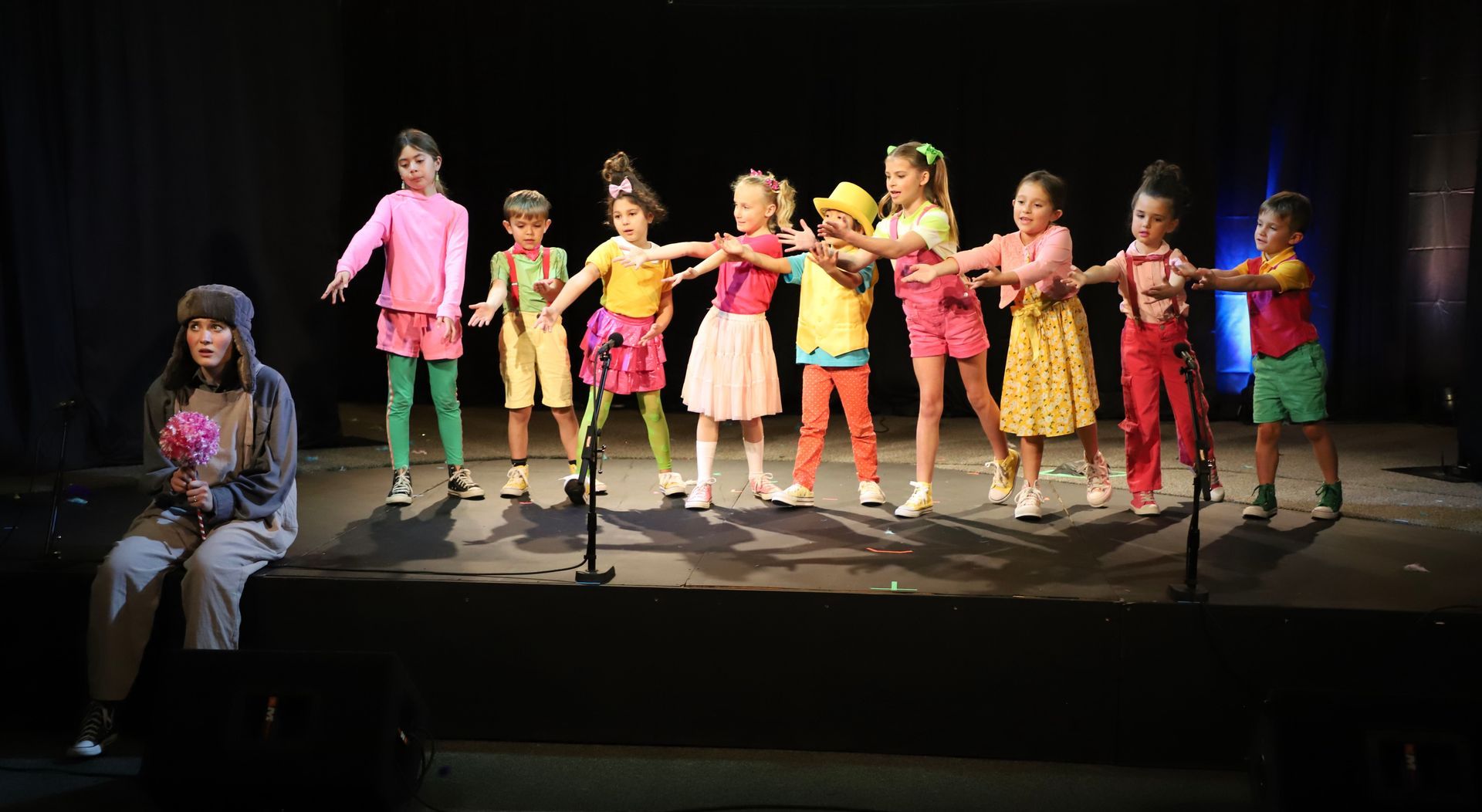 A group of children are standing on a stage holding hands.