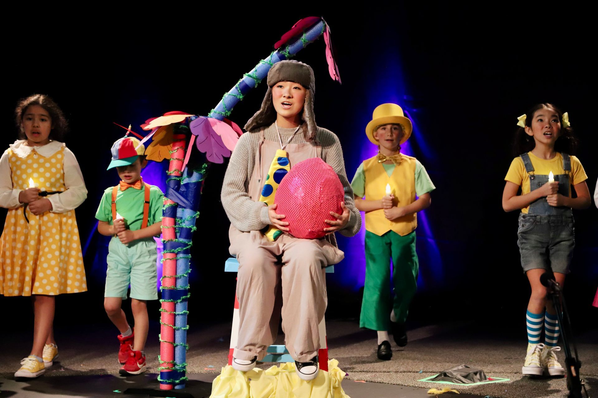A group of children are standing on a stage holding candles.