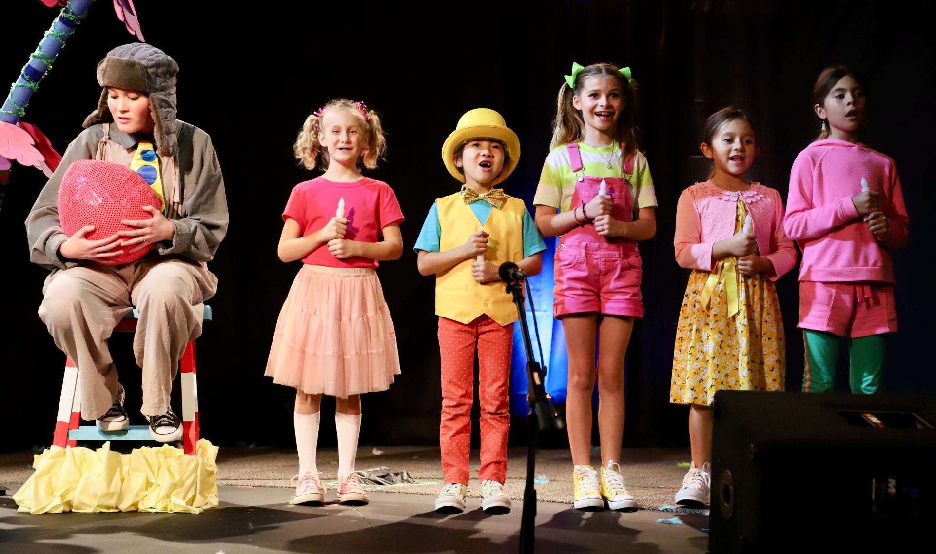 A group of children are standing on a stage singing into microphones.