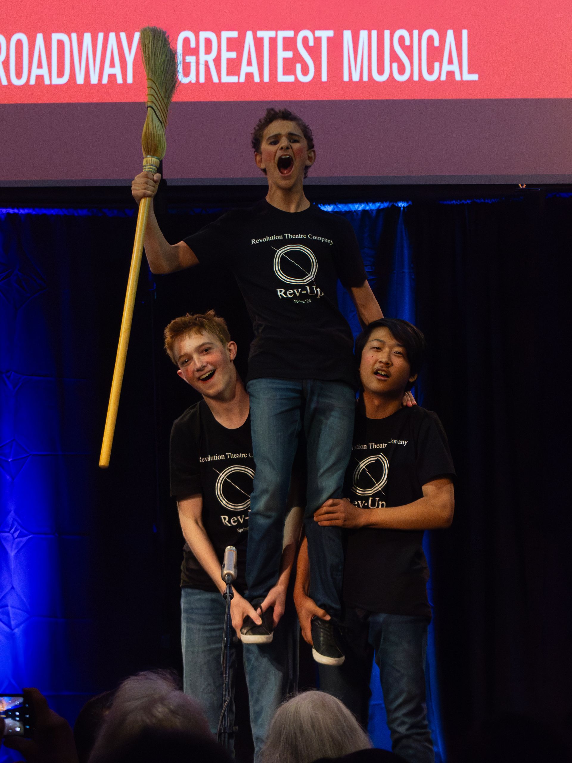 A group of people standing in front of a sign that says broadway greatest musical