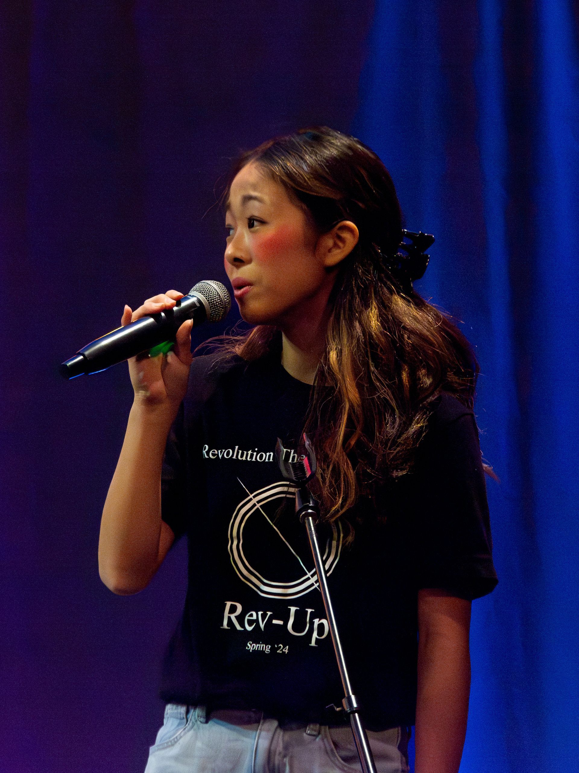 A woman singing into a microphone wearing a rev-up shirt