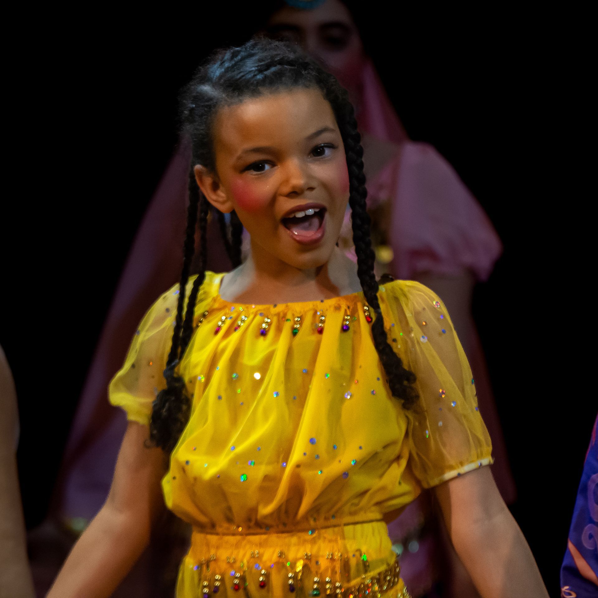 A young girl in a yellow dress is dancing on a stage.