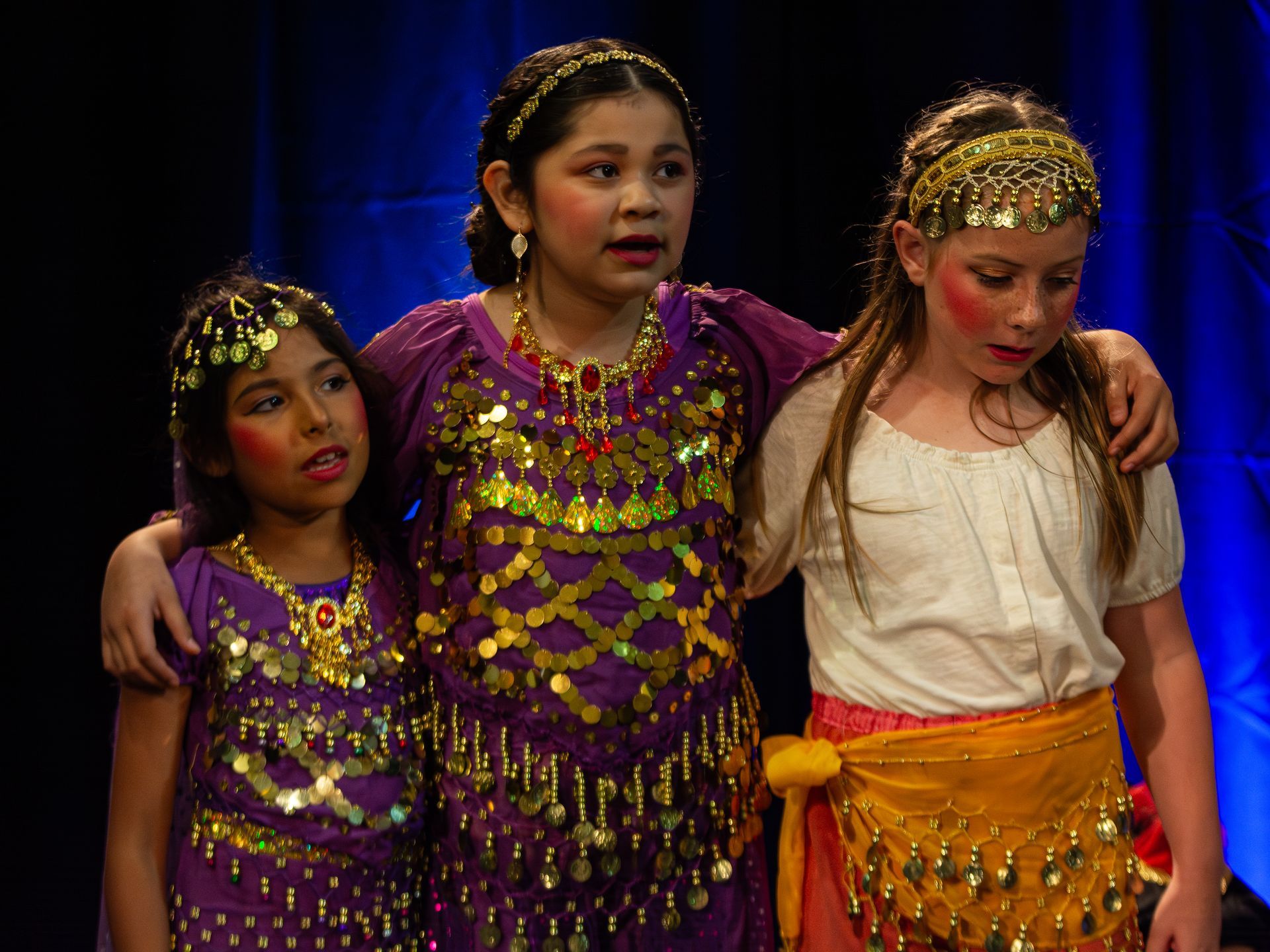 Three young girls in costume are standing next to each other on a stage.