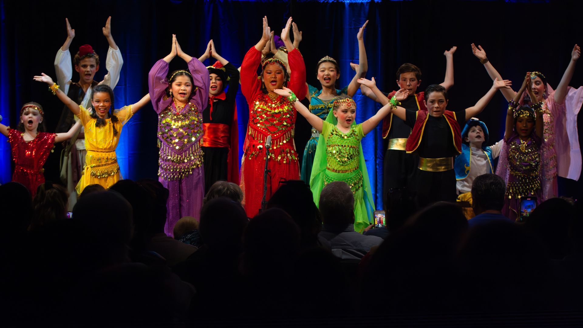 A group of children are dancing on a stage in front of a crowd.