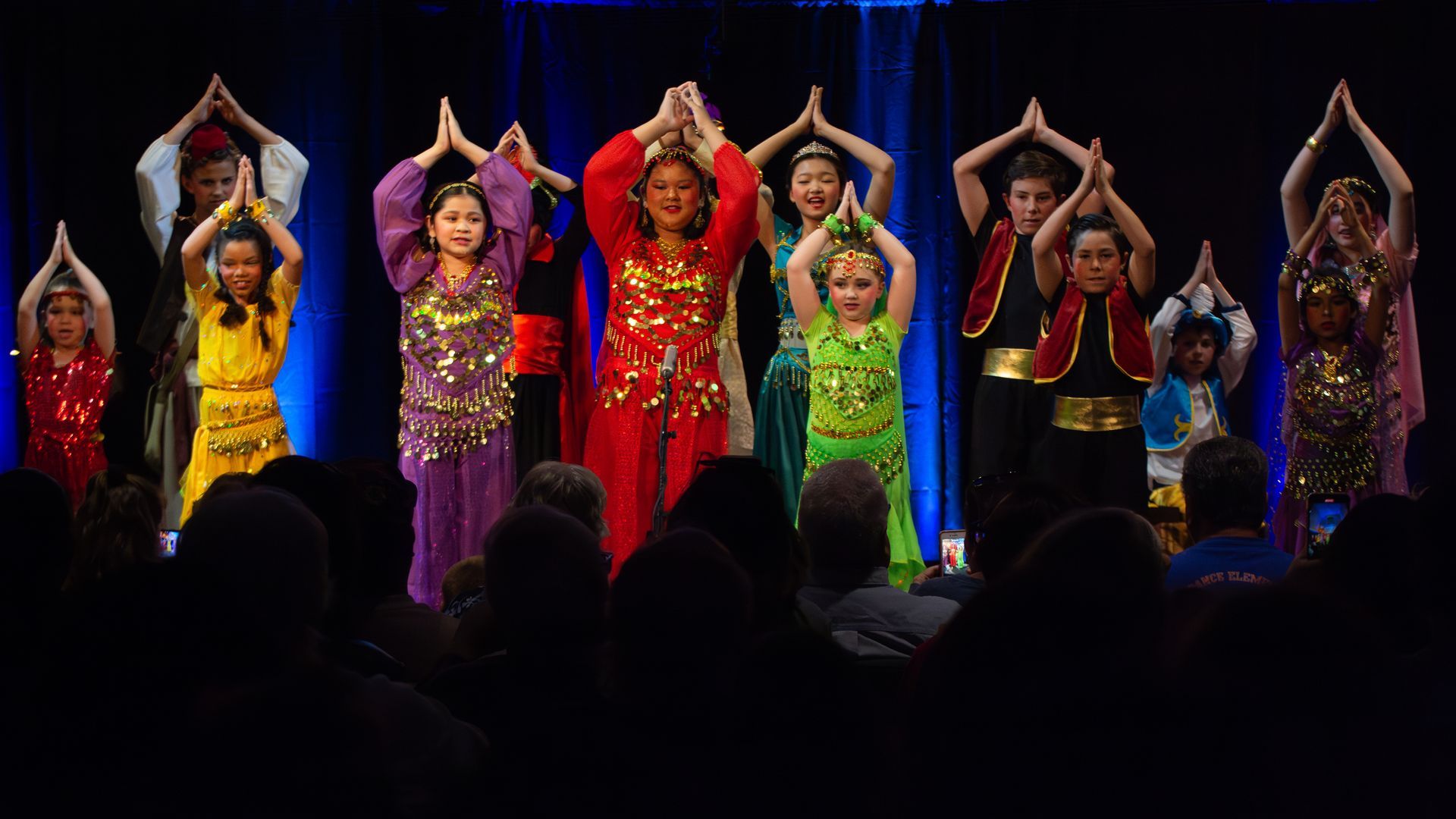 A group of children are dancing on a stage in front of a crowd.