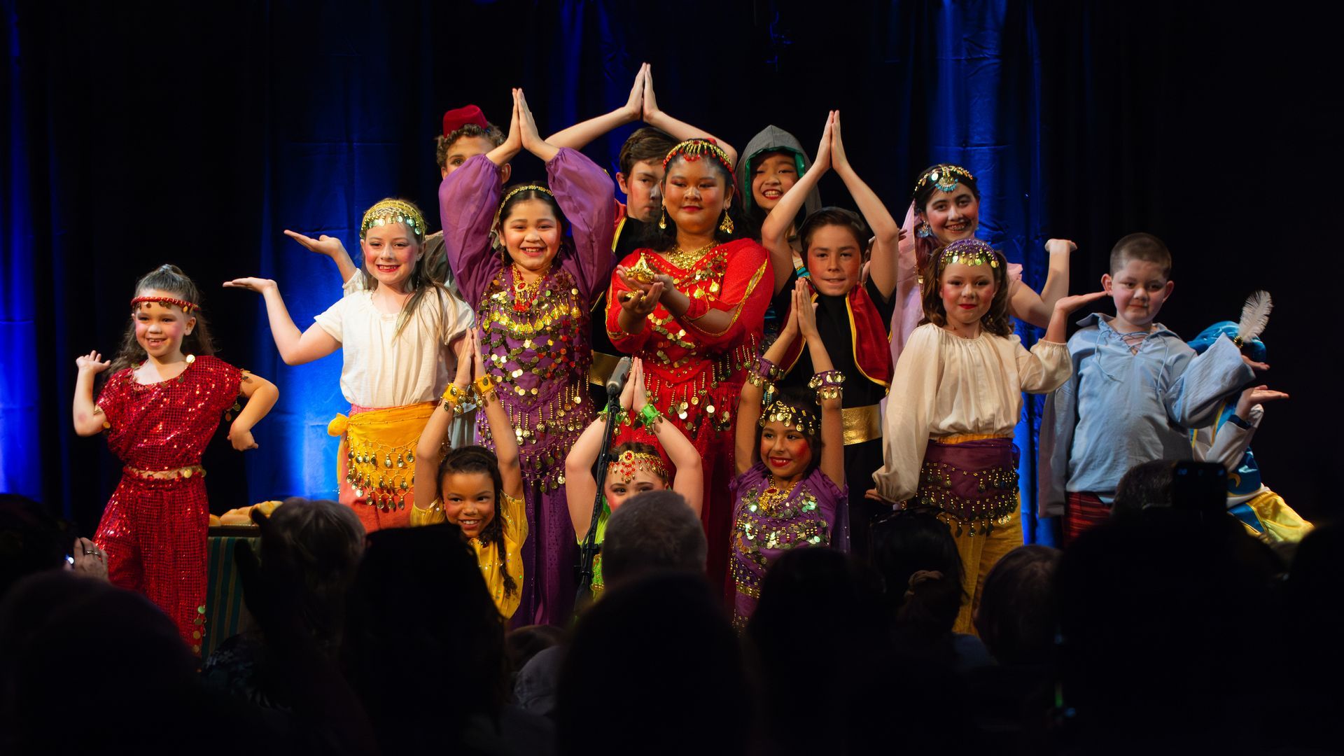 A group of children are dancing on a stage in front of a crowd.