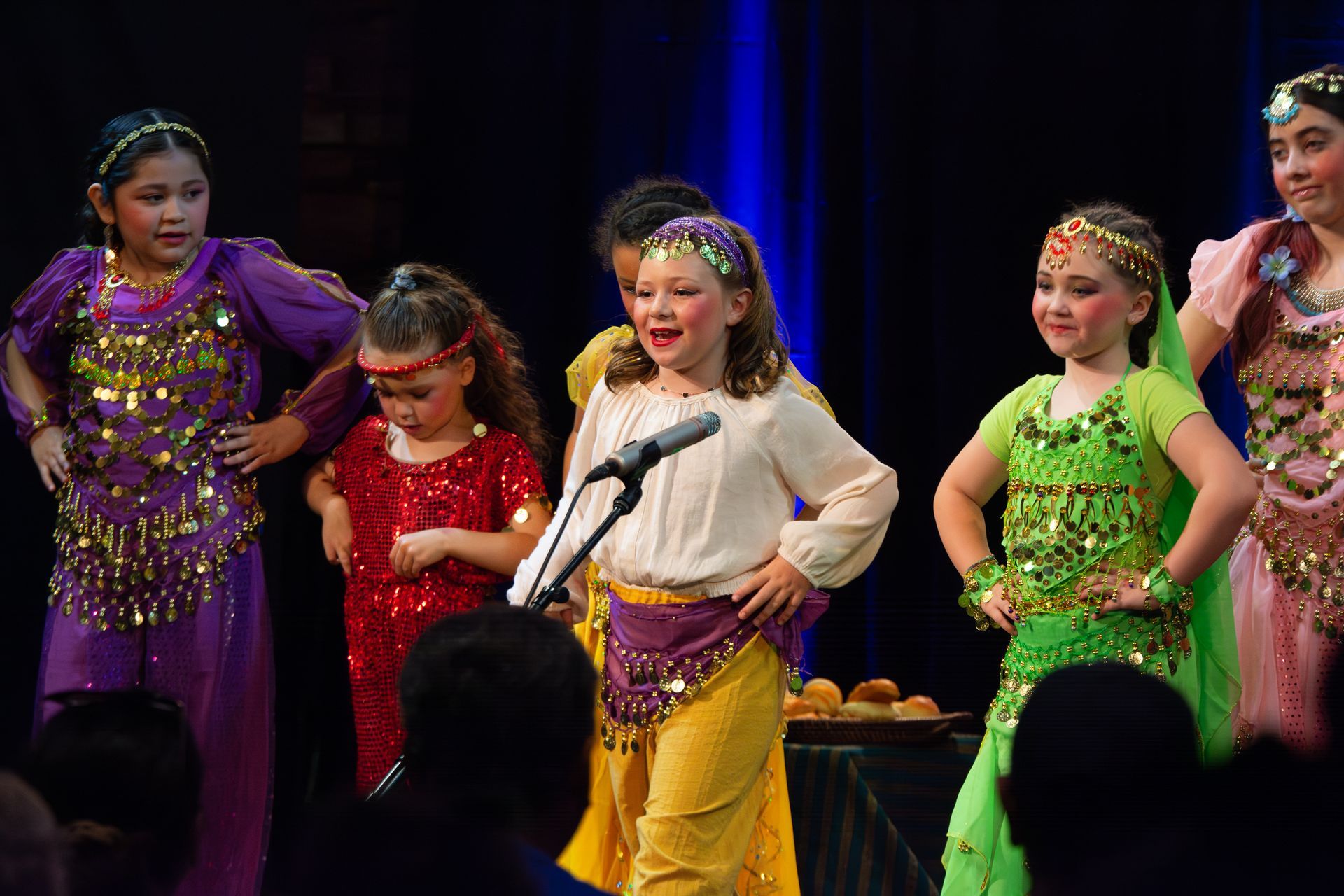 A group of young girls are standing in front of a microphone on a stage.
