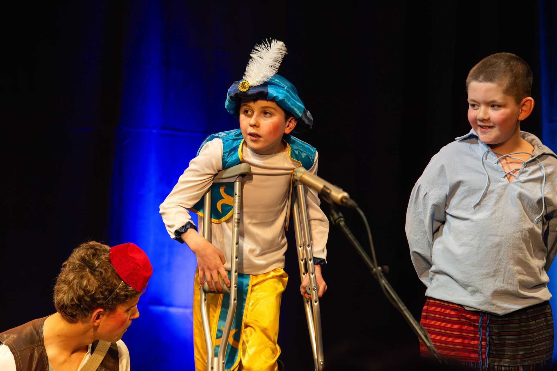 A boy with crutches is standing in front of a microphone on a stage.