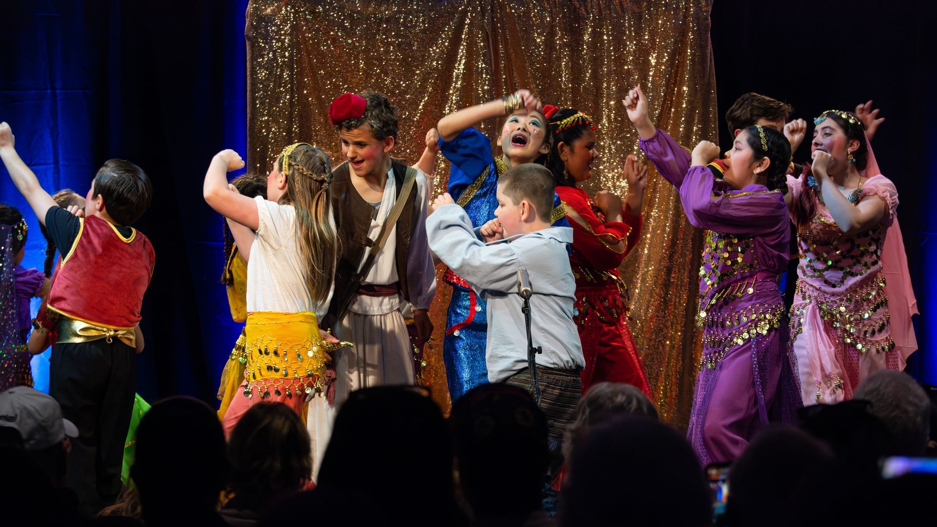 A group of children are dancing on a stage in front of a crowd.