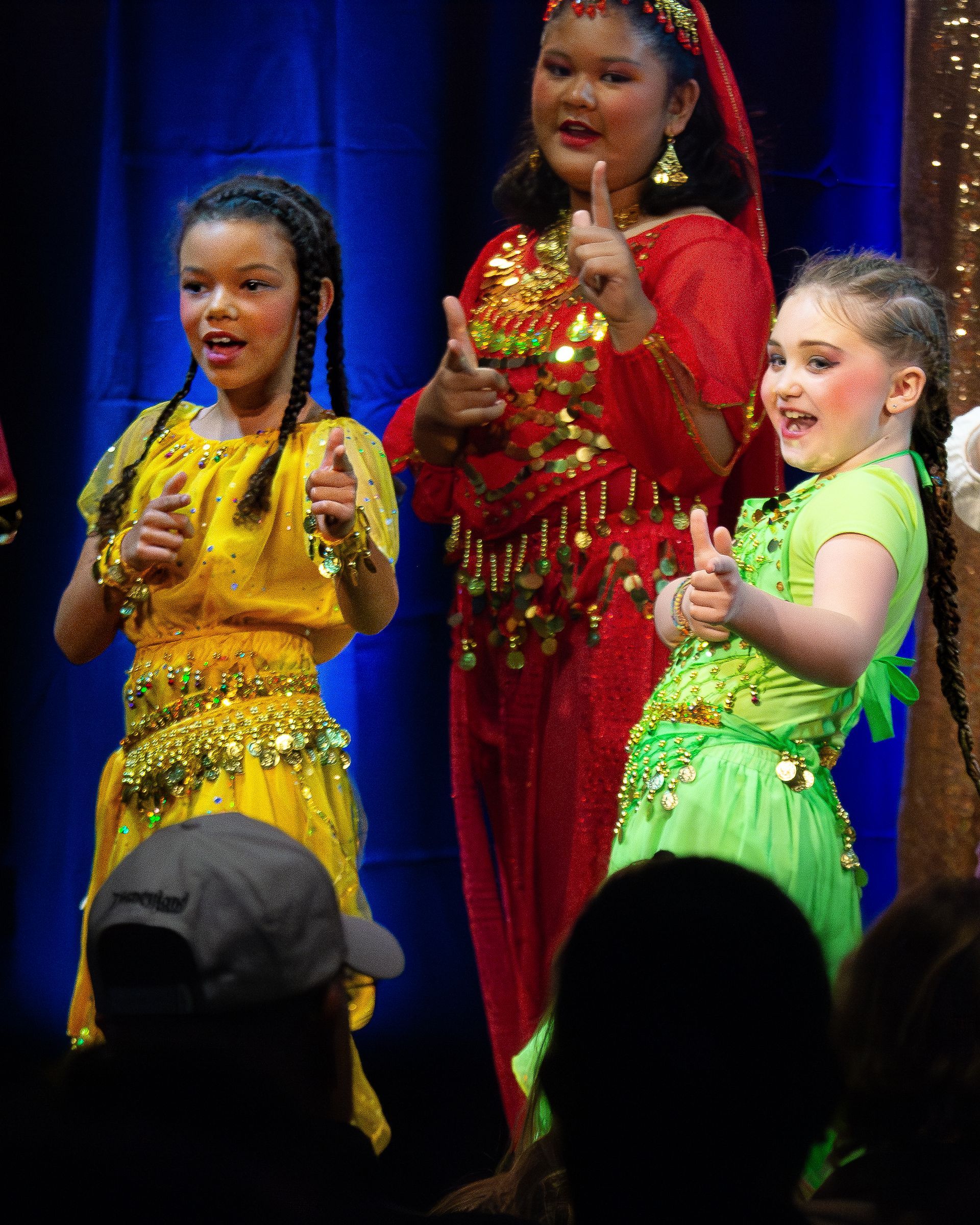 Three young girls are giving a thumbs up on a stage.