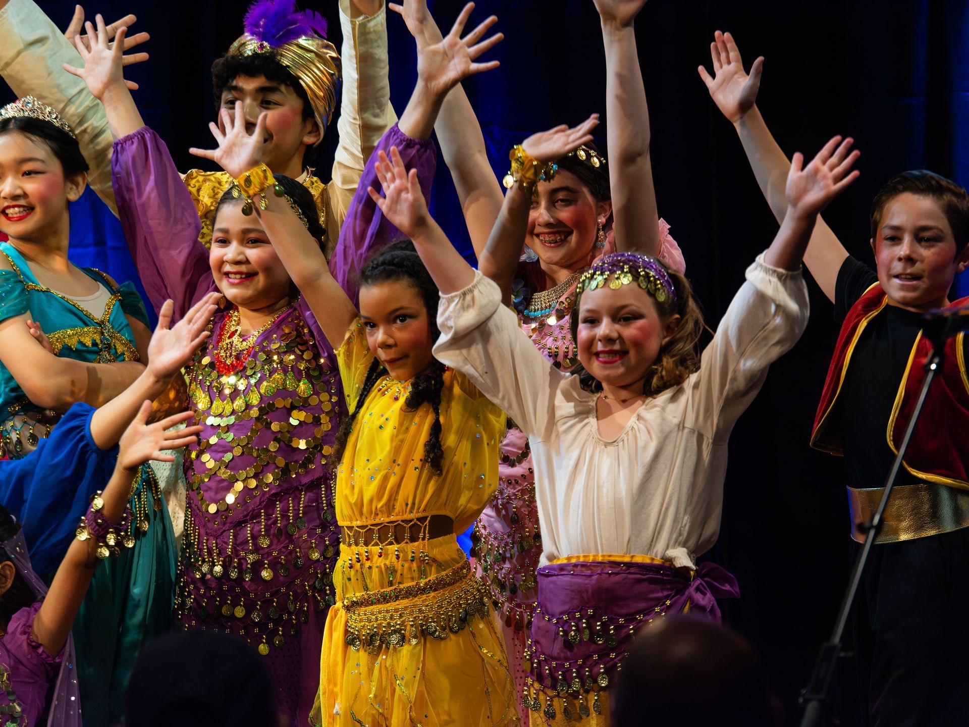 A group of children are performing on stage with their hands in the air