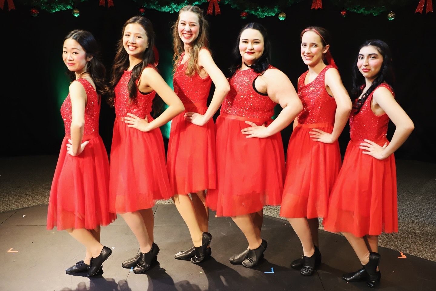 A group of young women in red dresses are standing next to each other on a stage.