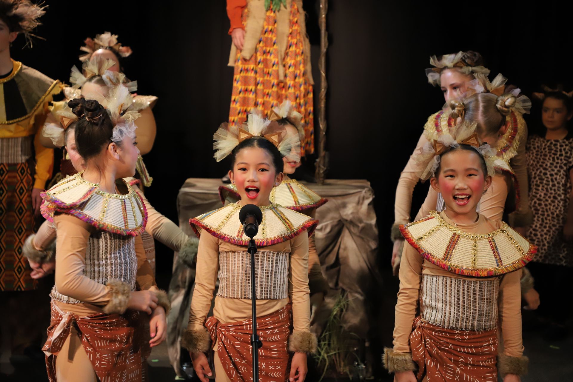 A group of young girls in costume are singing into a microphone.