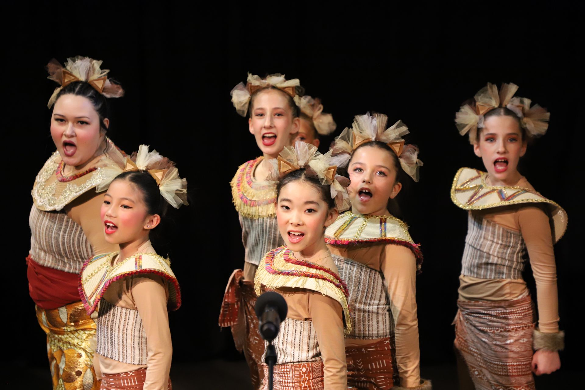 A group of young girls are singing into a microphone on a stage.