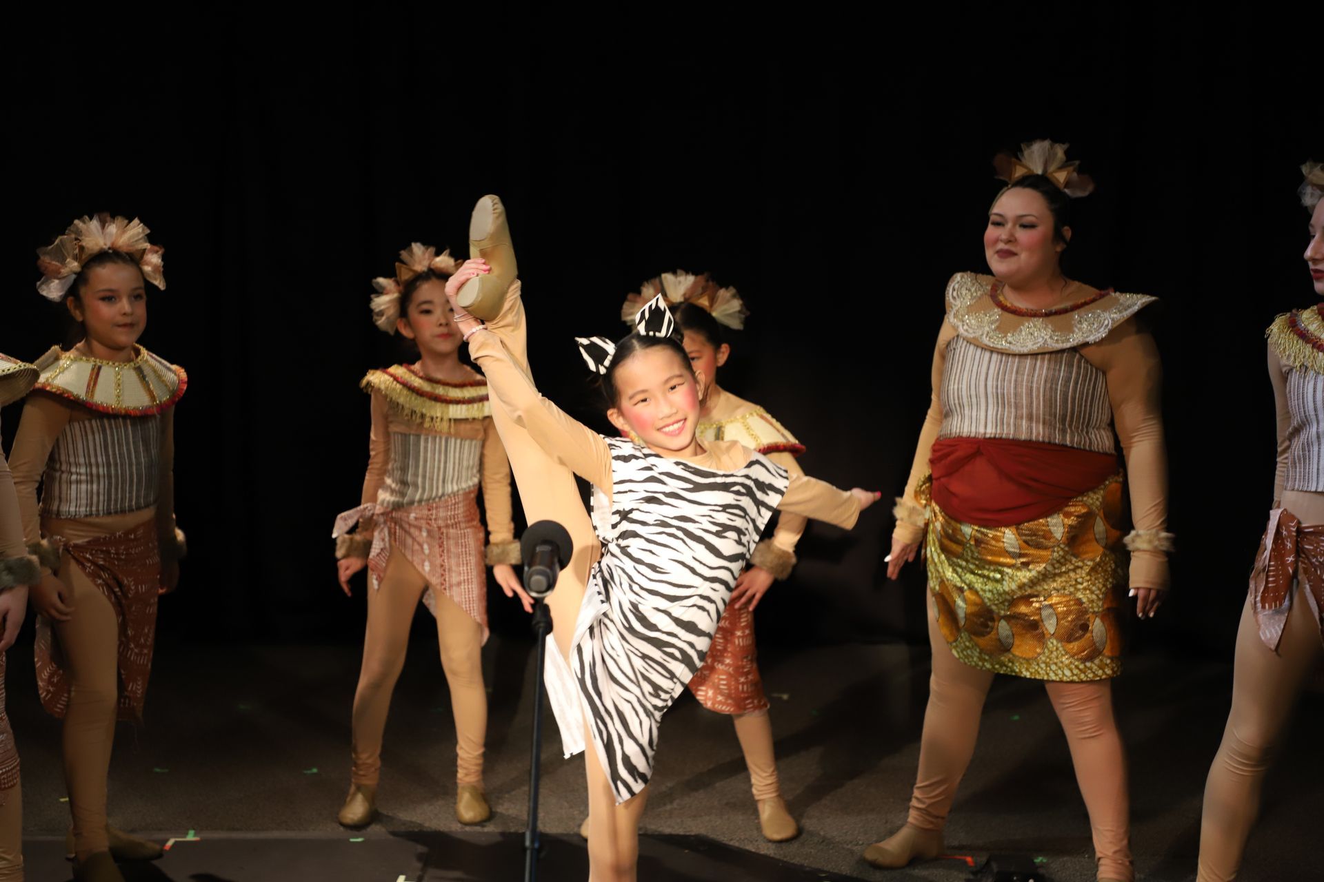 A group of young girls in costume are dancing on a stage.