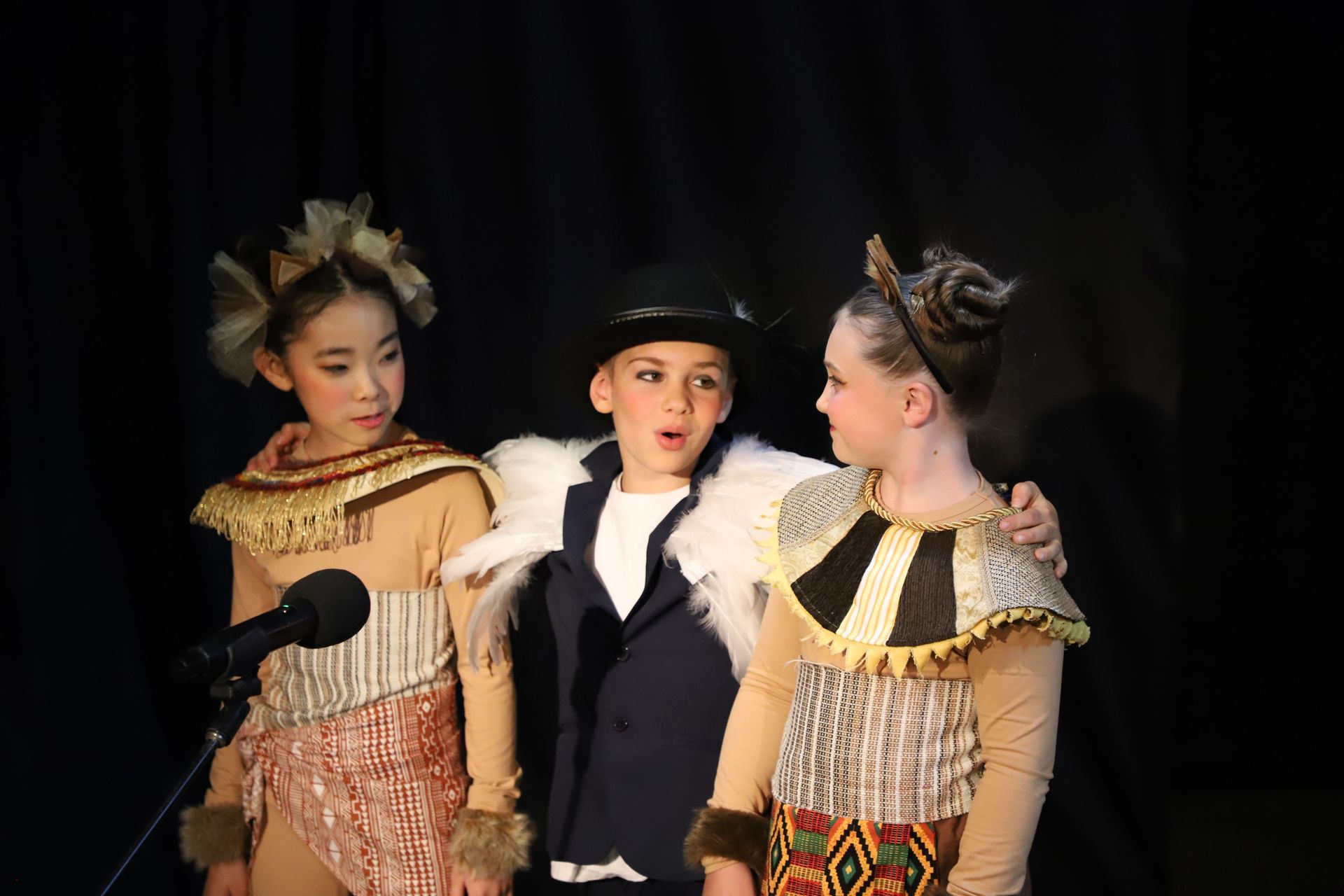 A boy and two girls are standing next to each other in front of a microphone.
