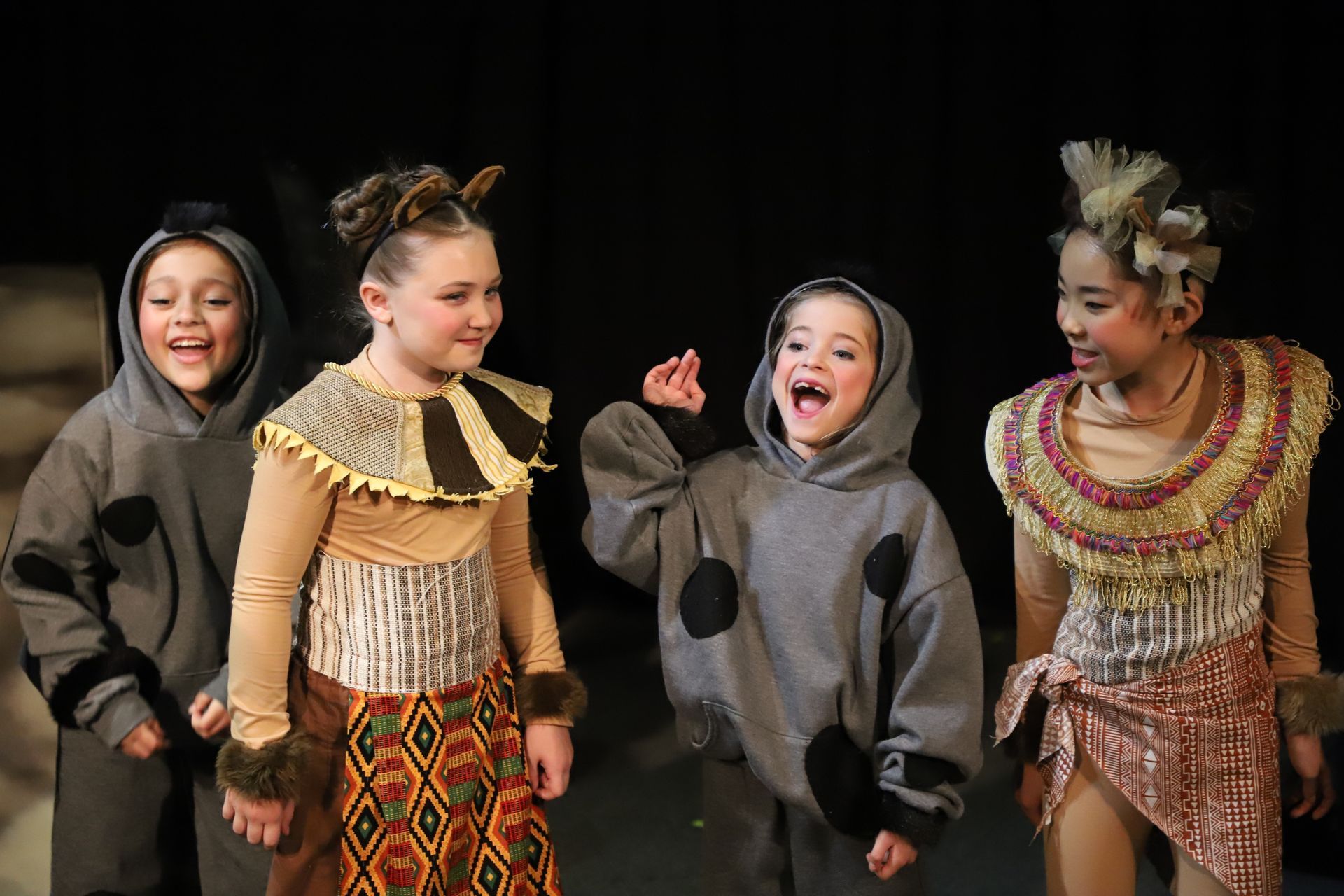 A group of children dressed in costumes are standing next to each other on a stage.