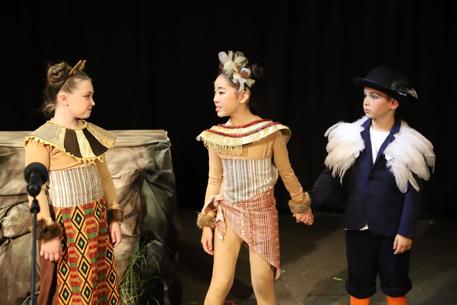 Three children in costume are standing next to each other on a stage.