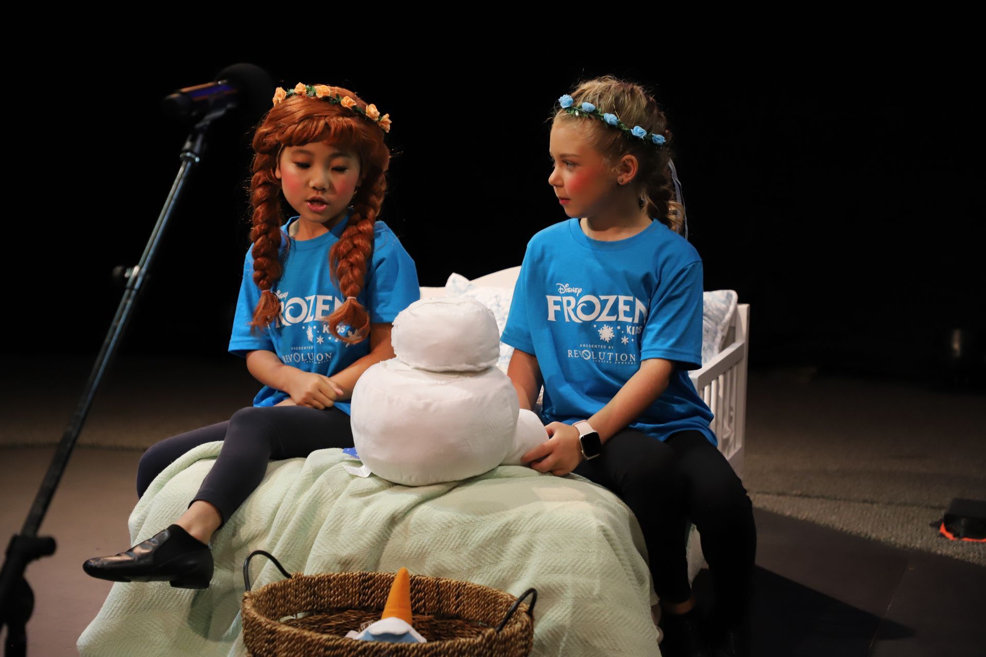 Two young girls are sitting on a bed with a snowman.