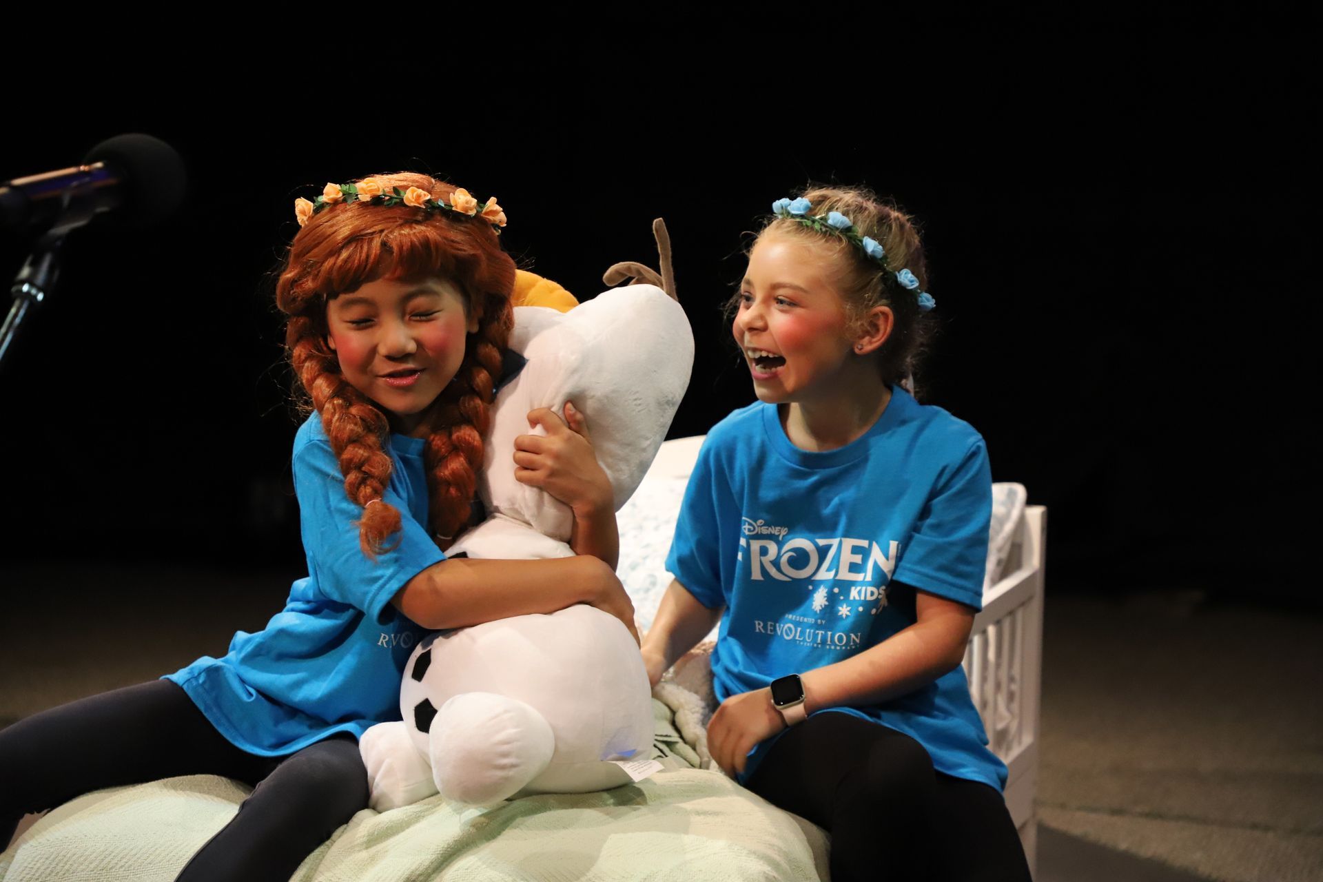 Two young girls are sitting next to each other on a bed holding a stuffed animal.