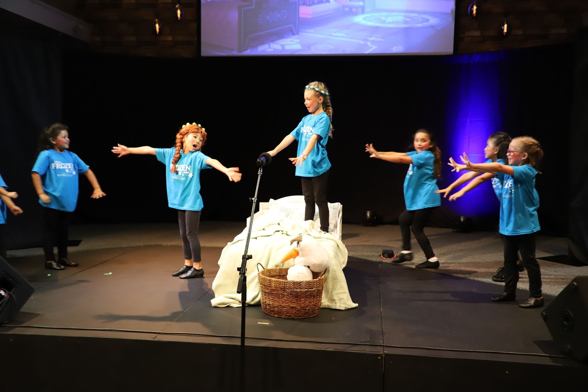 A group of children in blue shirts are performing on a stage.