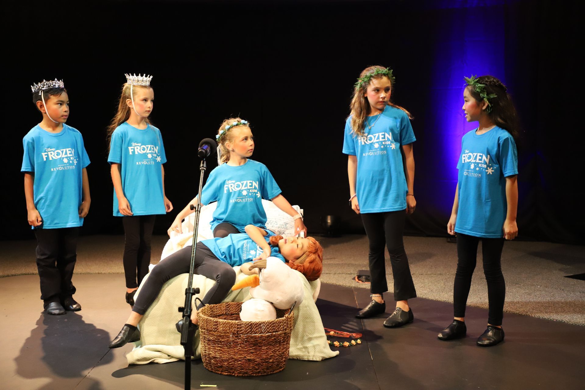 A group of young girls are standing around a microphone on a stage.