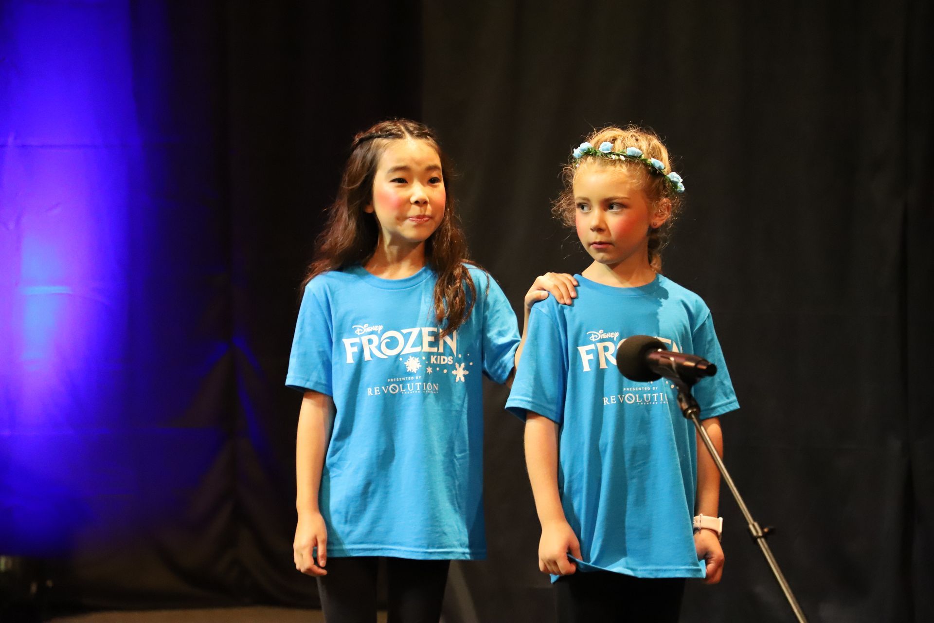 Two young girls are singing into a microphone on a stage.