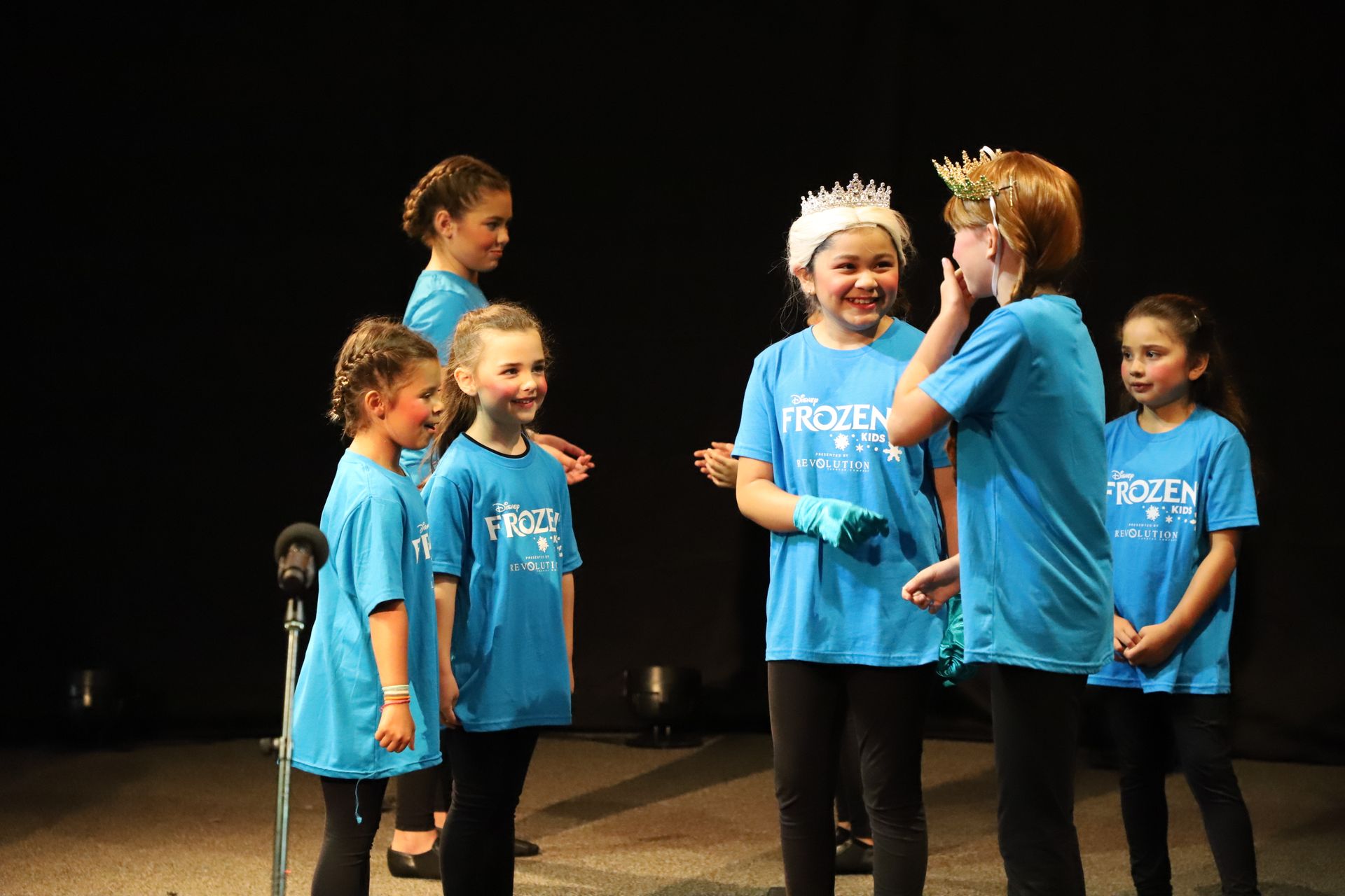 A group of young girls in blue shirts are standing on a stage.