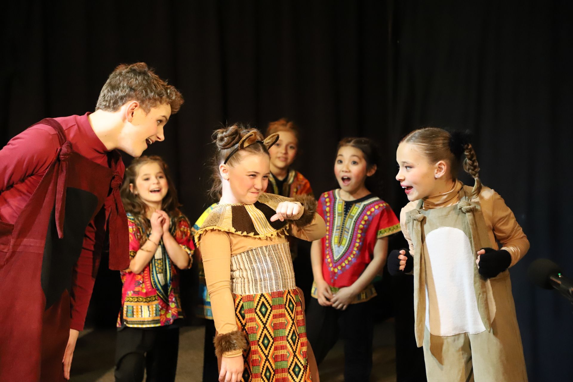A group of children in costume are standing on a stage talking to each other.