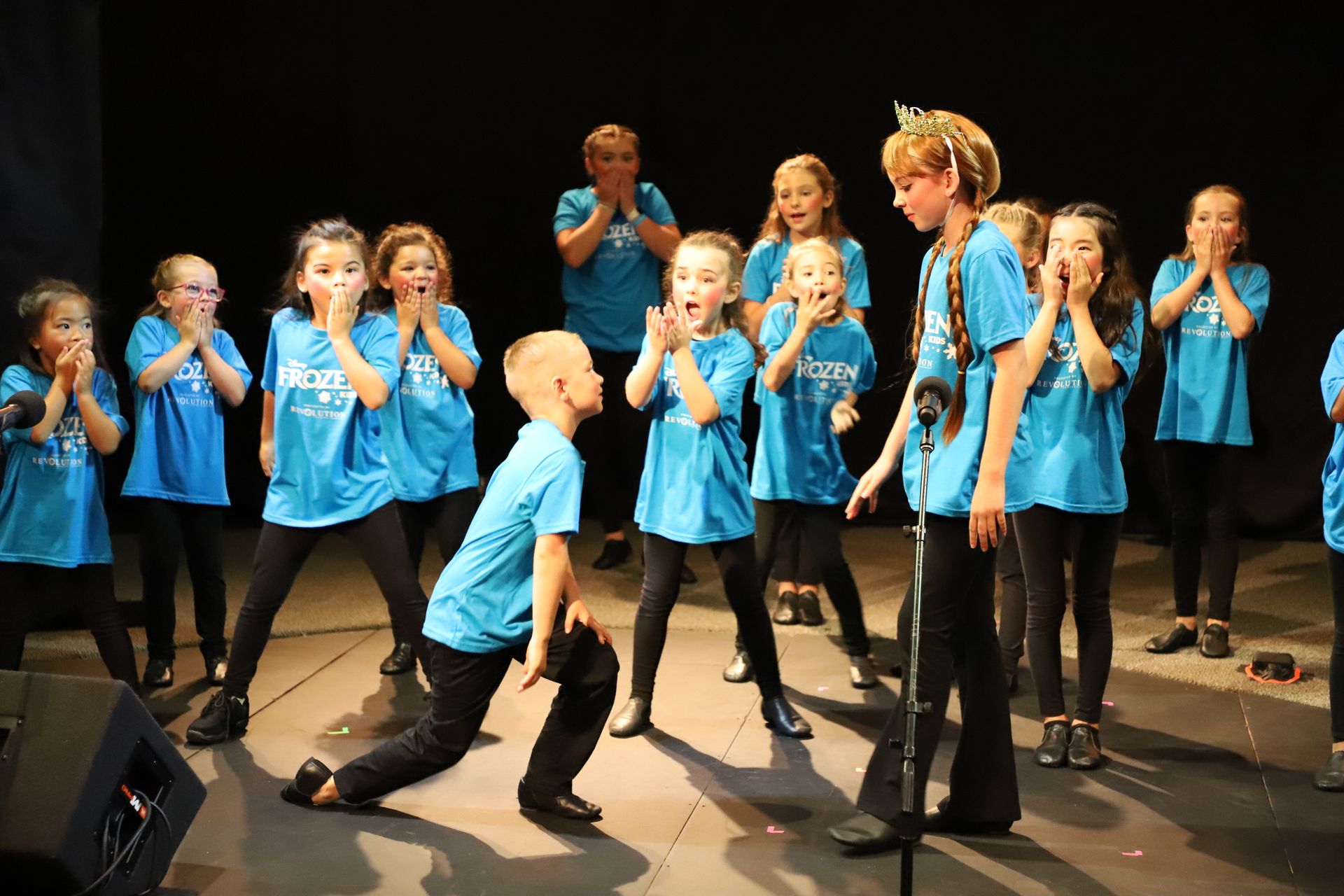 A group of children in blue shirts are dancing on a stage.