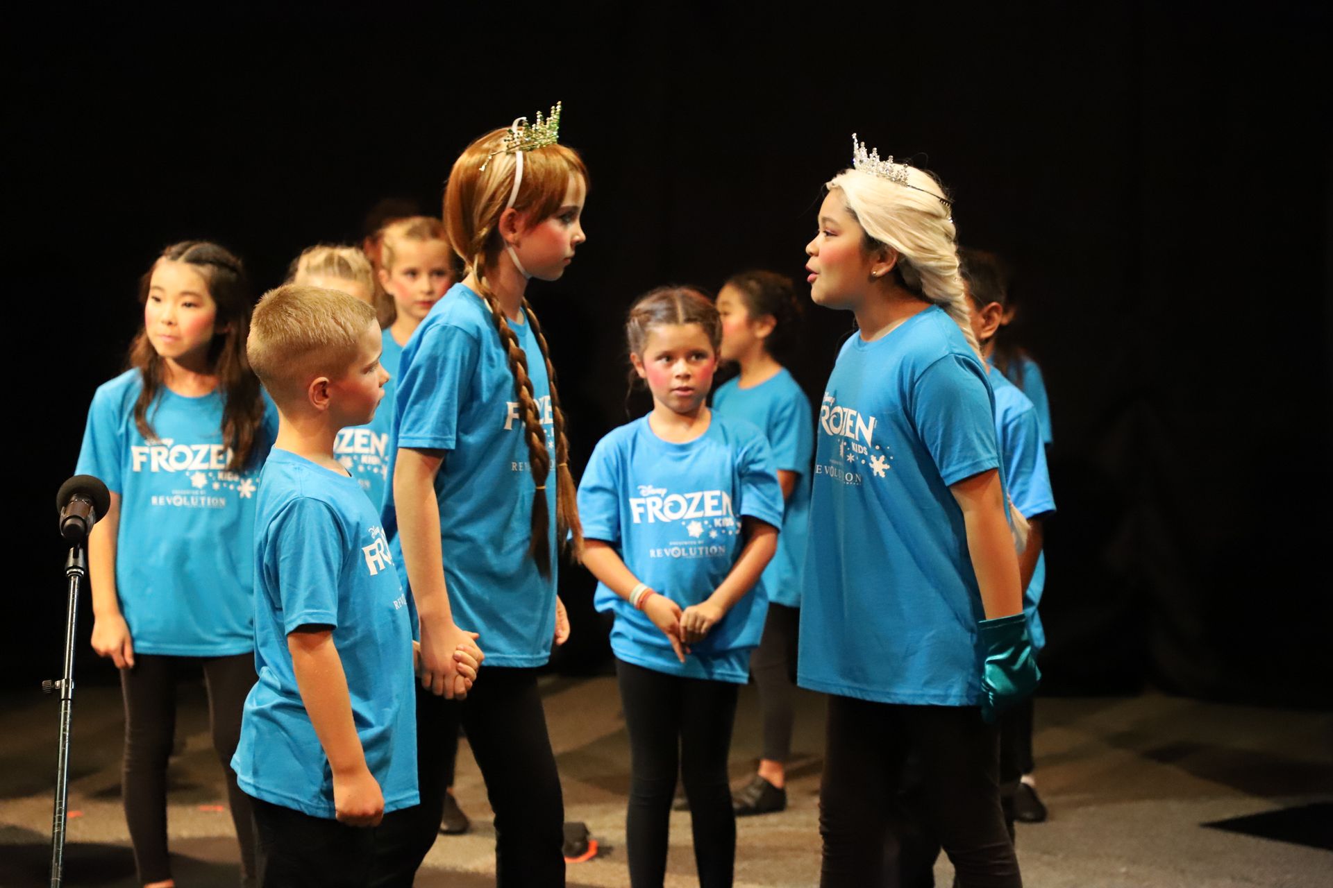 A group of children in blue shirts are standing on a stage.